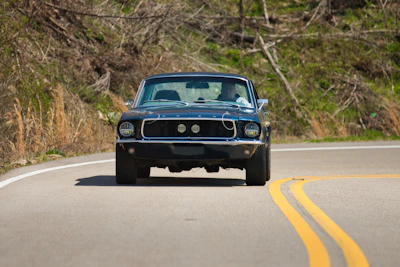 A vintage blue car drives on a winding road.