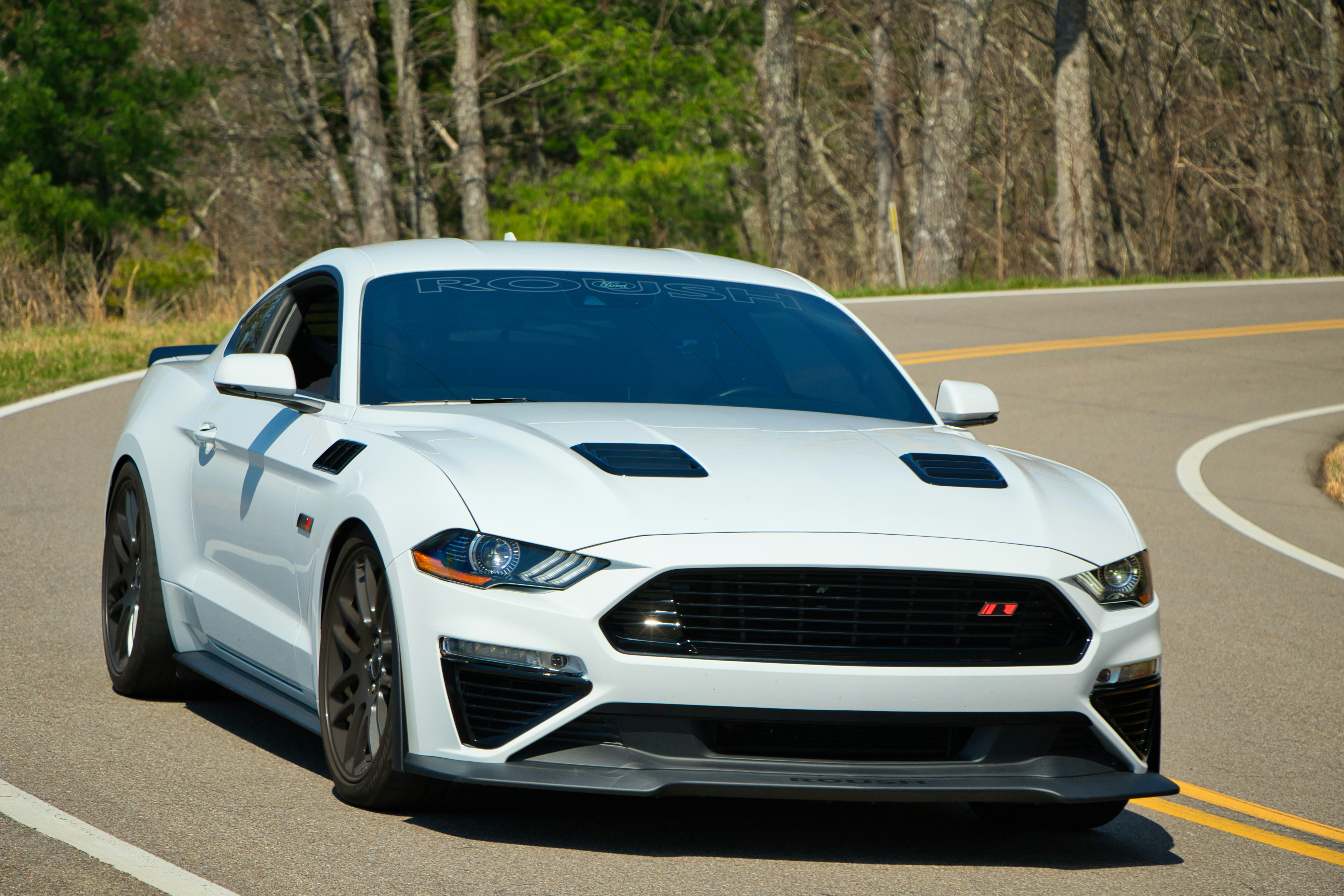 Ein weißer Ford Mustang fährt auf einer kurvigen Straße.
