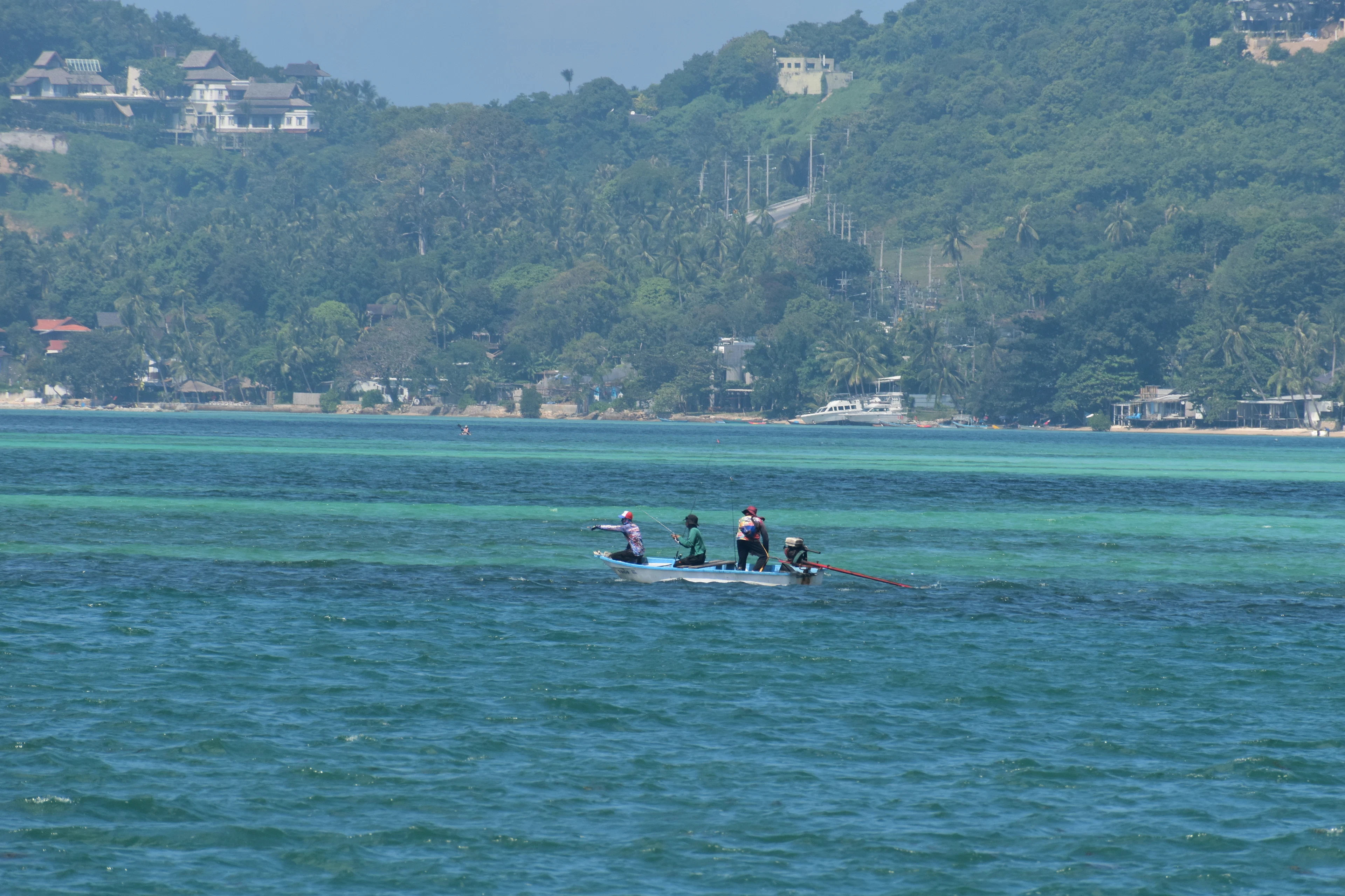 A small boat with people on clear blue water below the hills of Koh Samui