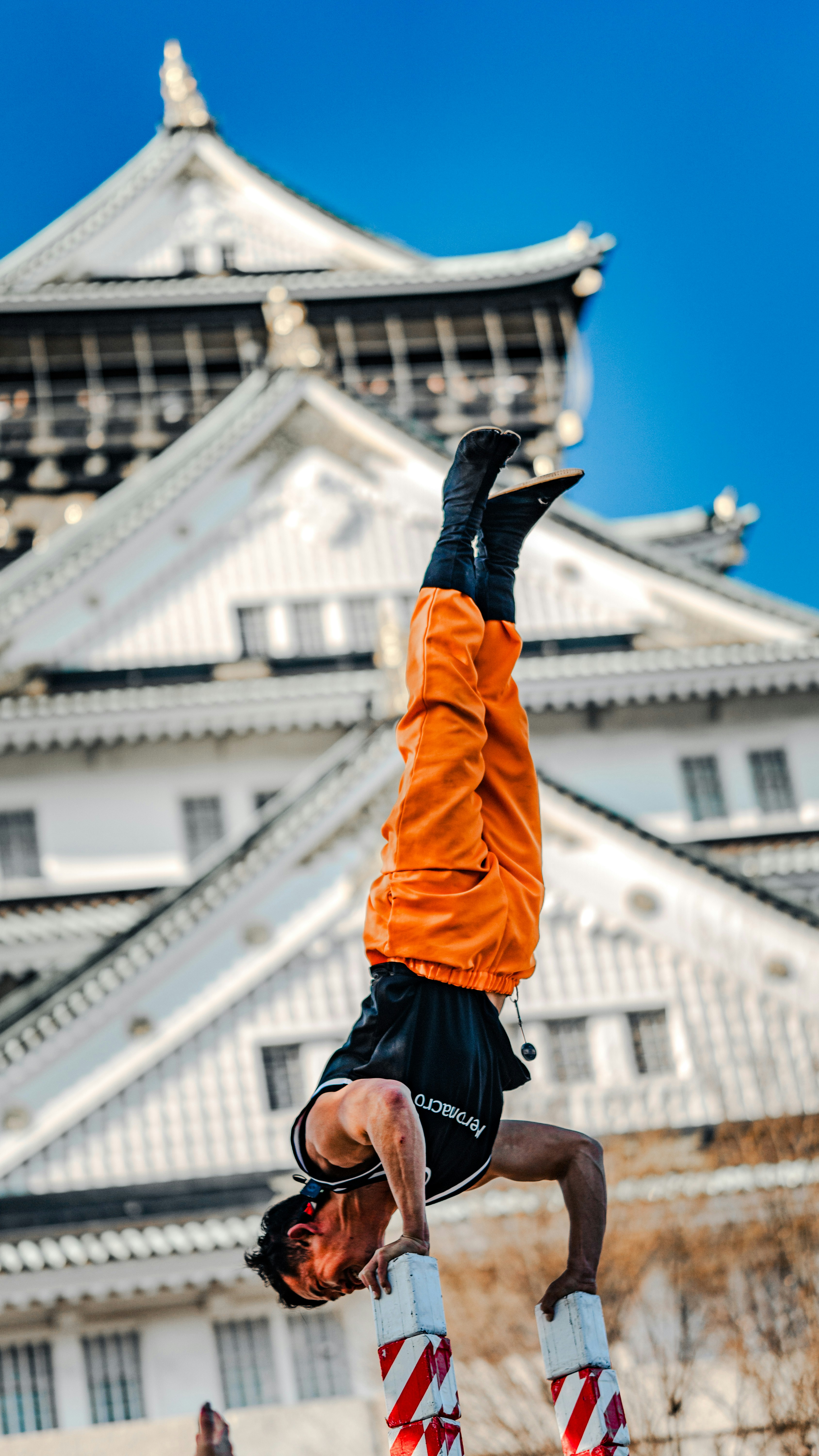 A man performs a handstand on pillars before a castle.