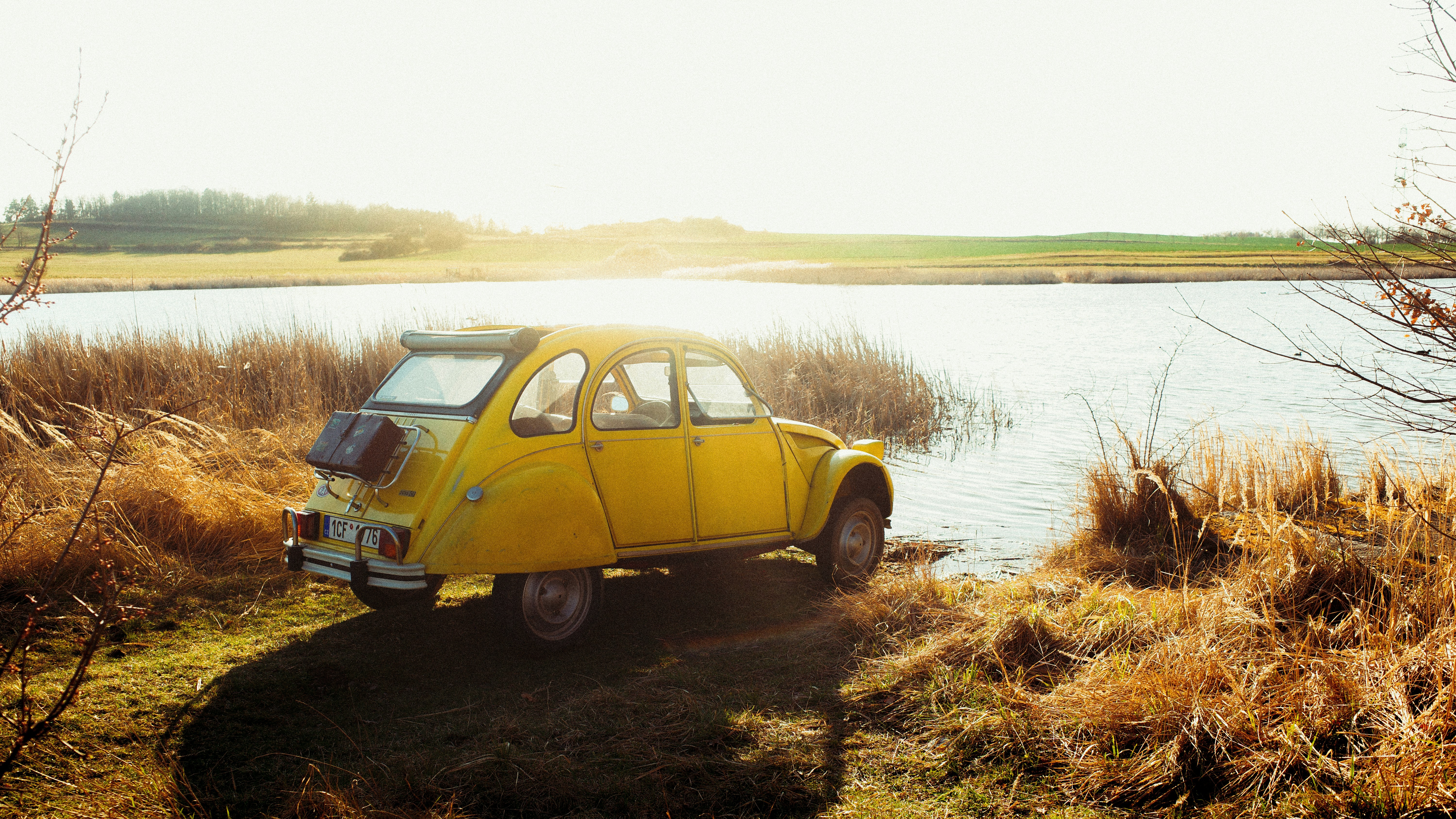 Sebuah mobil kuning diparkir di tepi danau saat matahari terbenam.