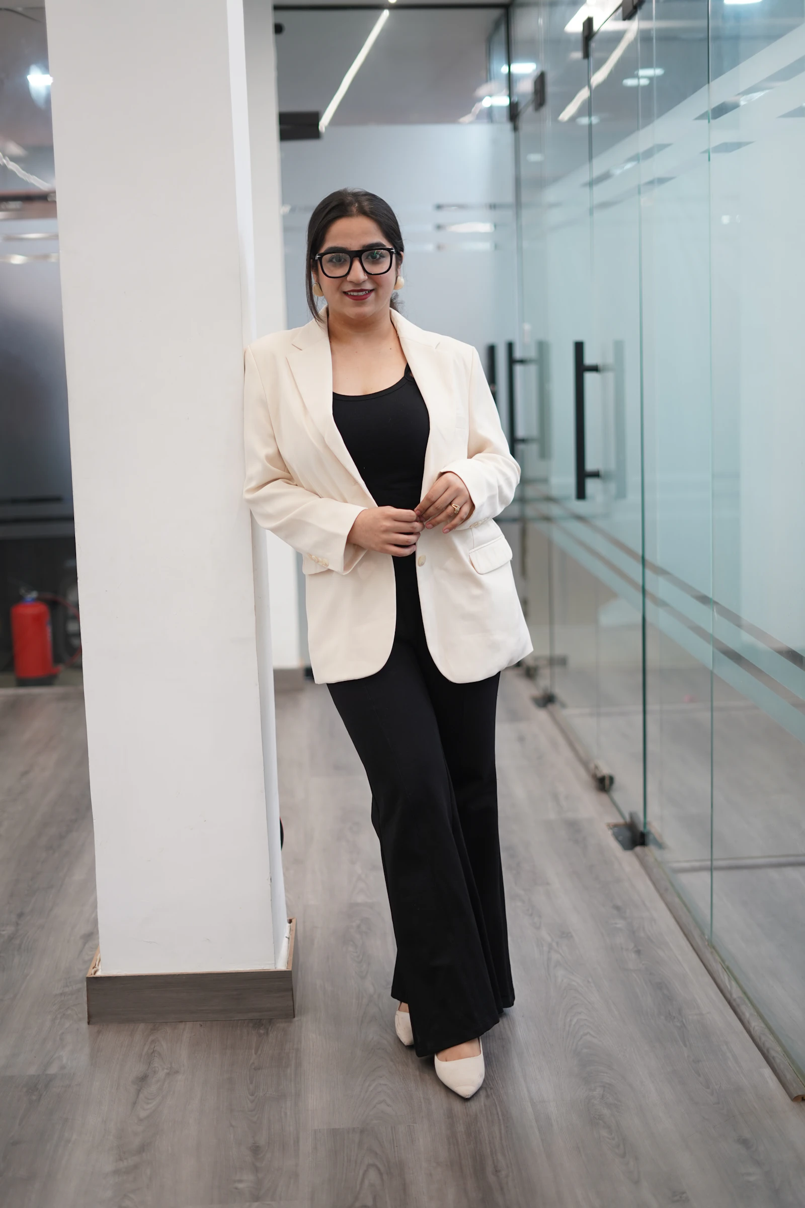 A smiling Indian finance professional in a cream blazer in a modern glass office