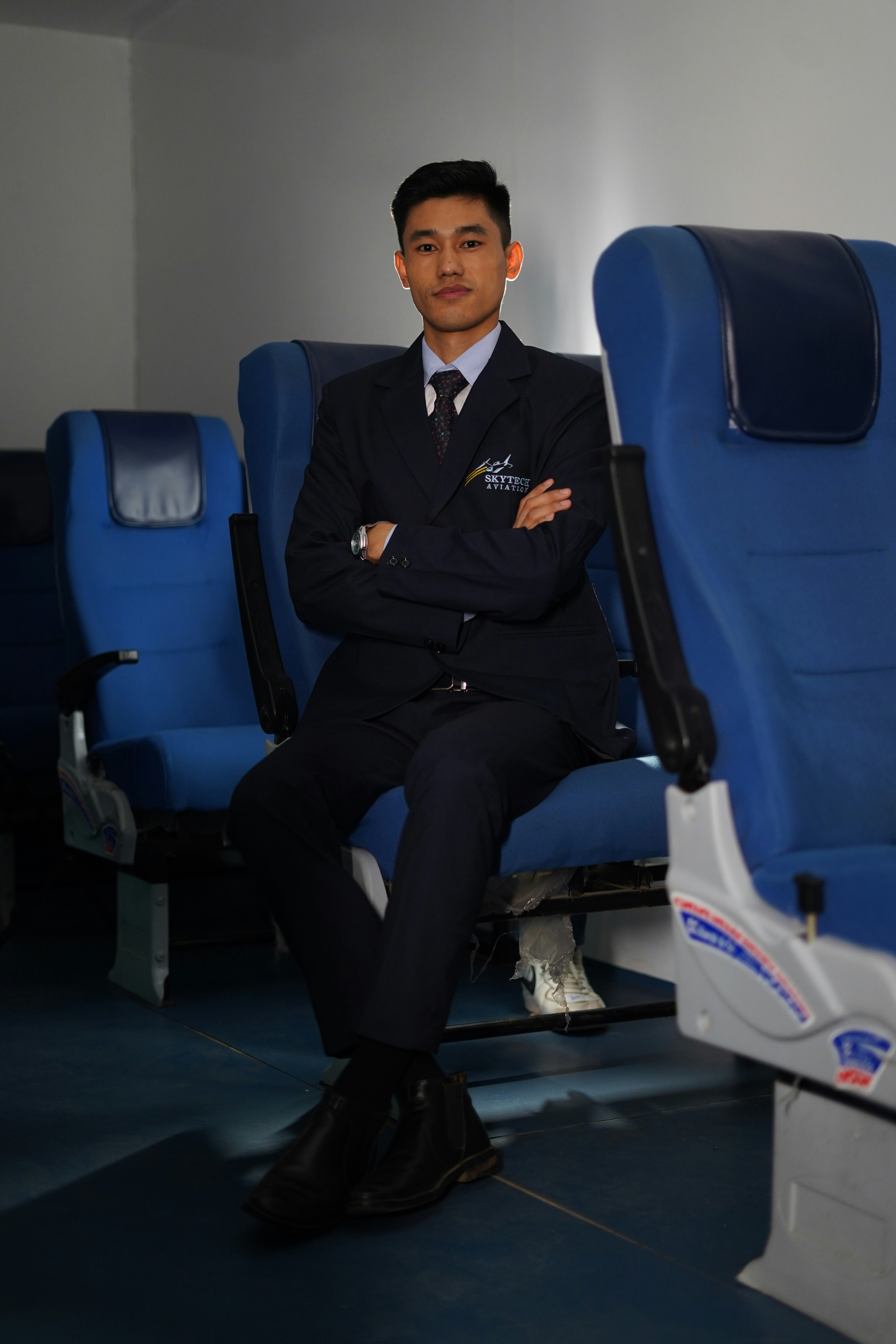 A young man in pilot uniform sits in airplane seats.