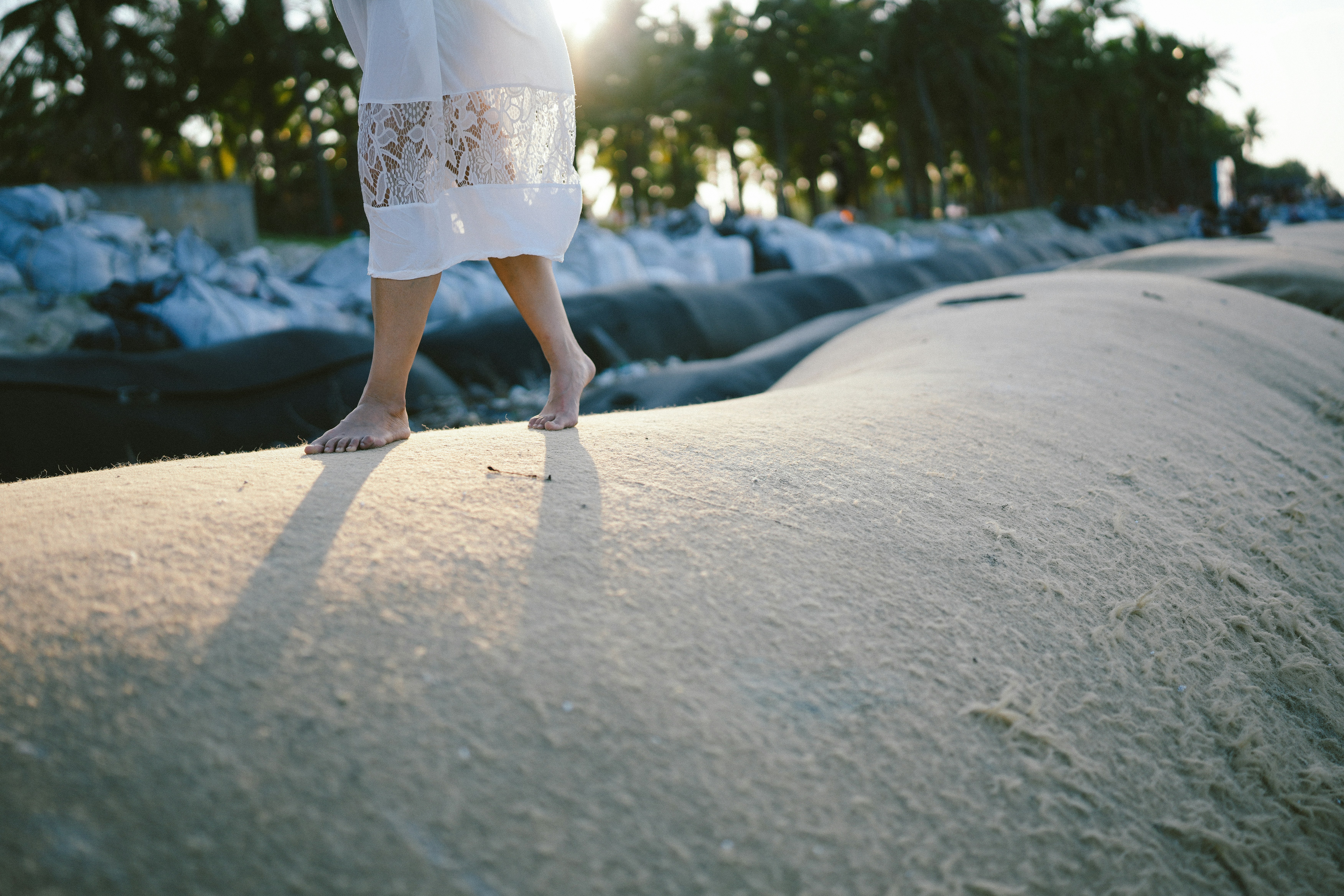 裸足の女性が夕暮れ時に砂の土手を歩く
