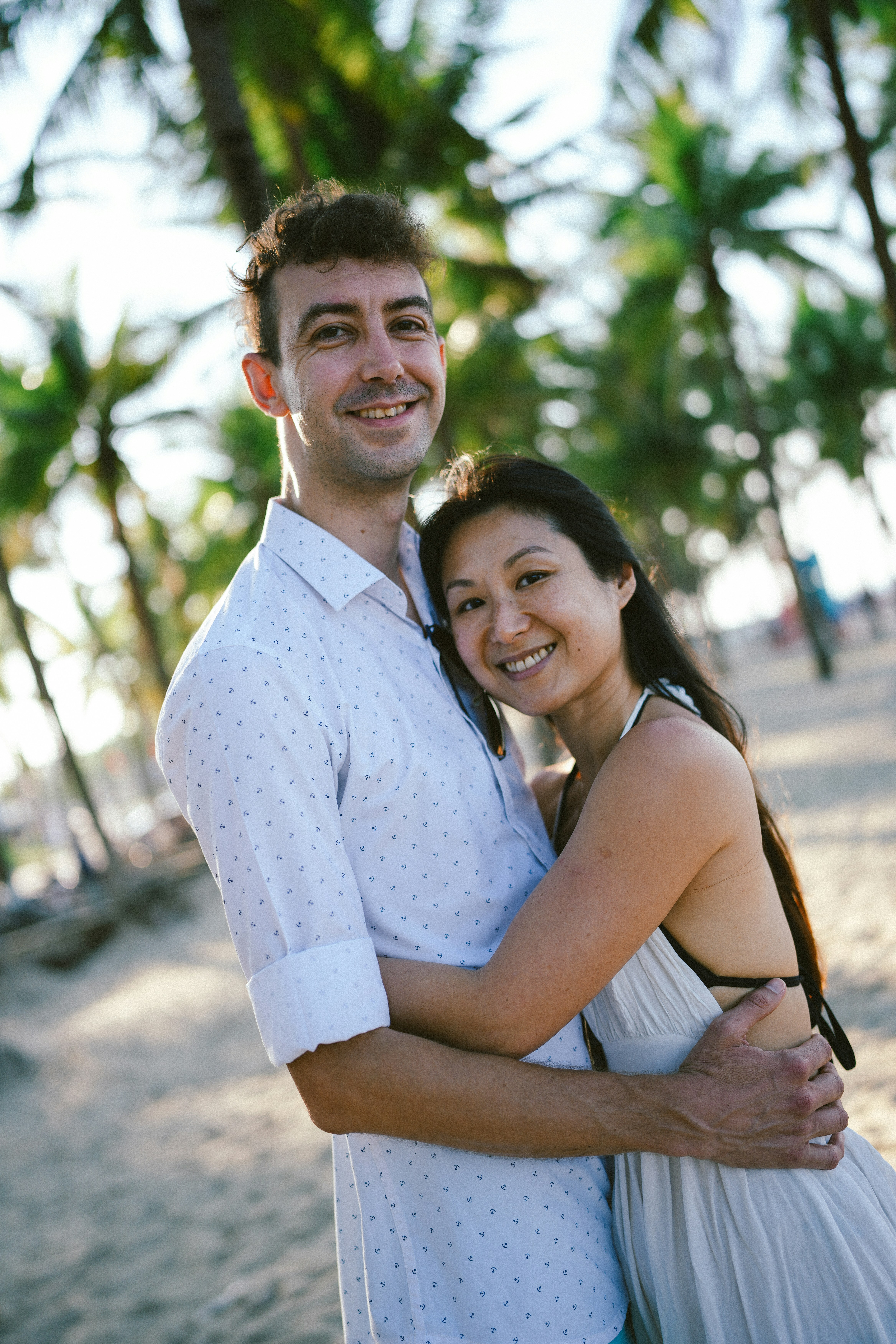 砂浜で笑顔のカップルが抱き合う。