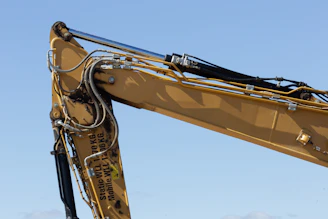 Close up of a yellow excavator arm against blue sky