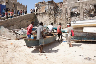 Men work on a boat on a sandy shore.