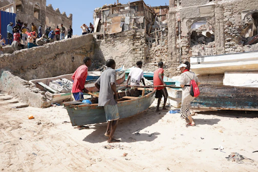 Men work on a boat on a sandy shore.