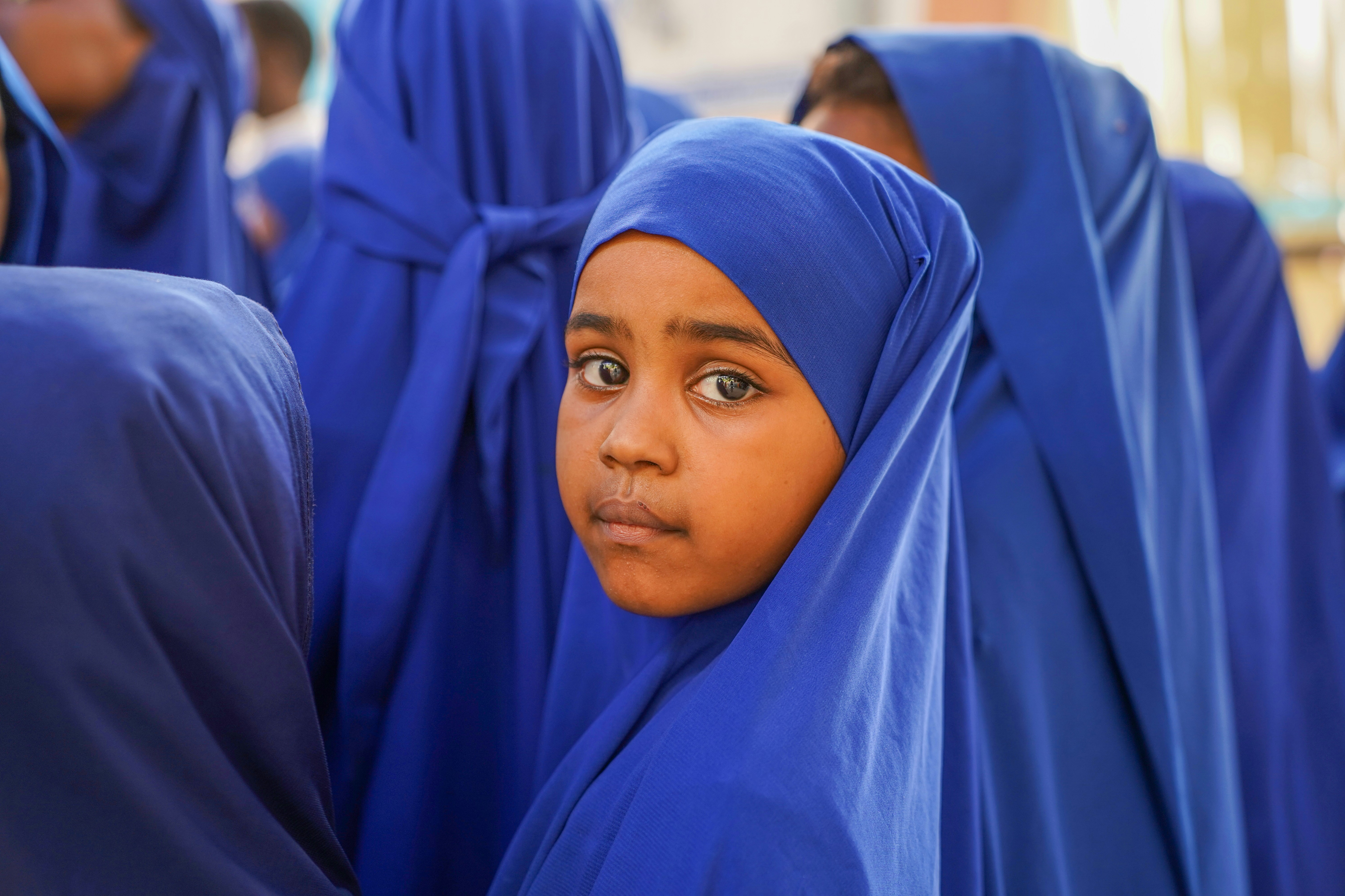 Garota jovem de hijab azul olha para a câmera.
