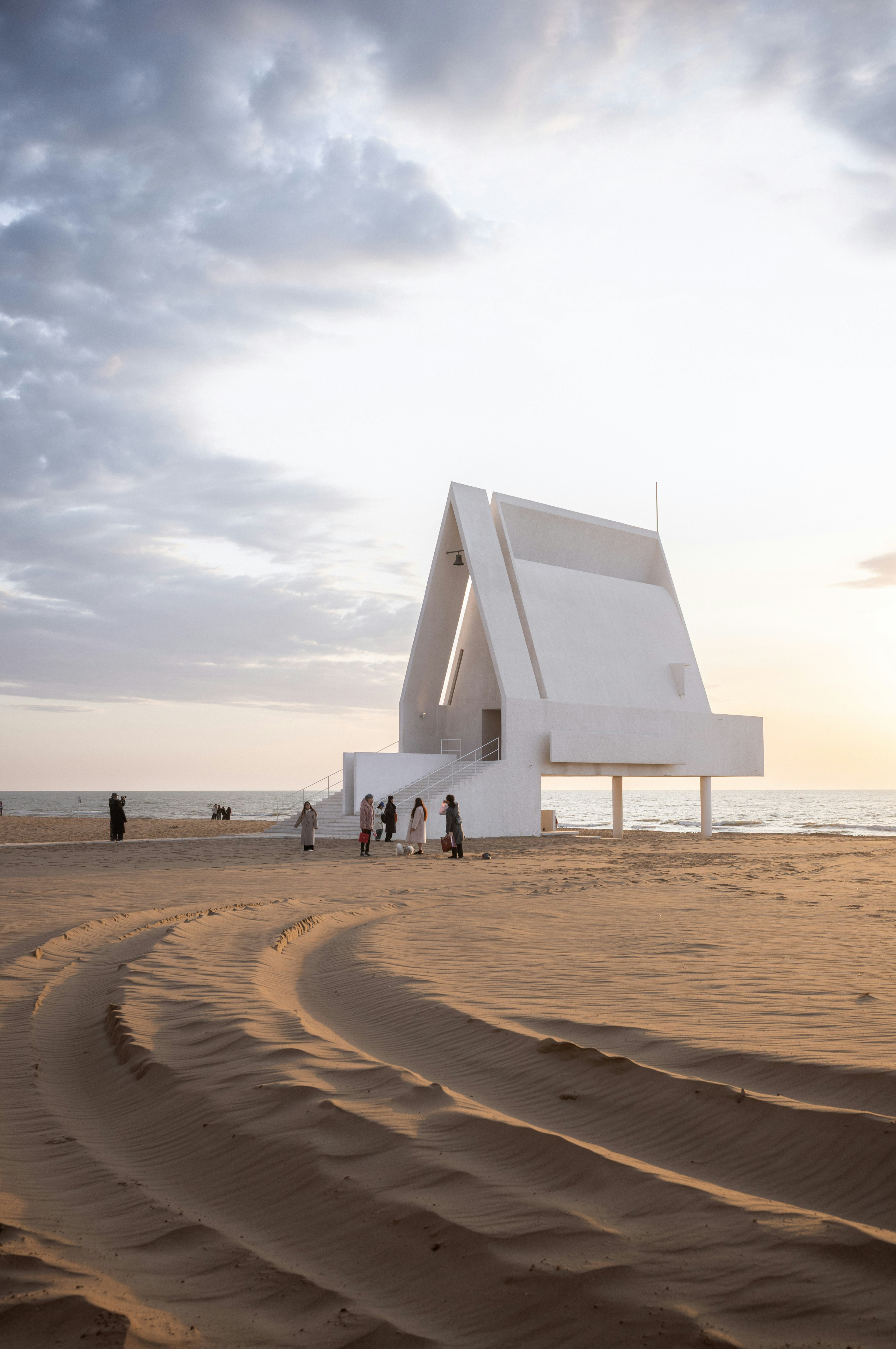 Modern white building on a sandy beach at sunset.