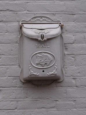White ornate mailbox mounted on a brick wall