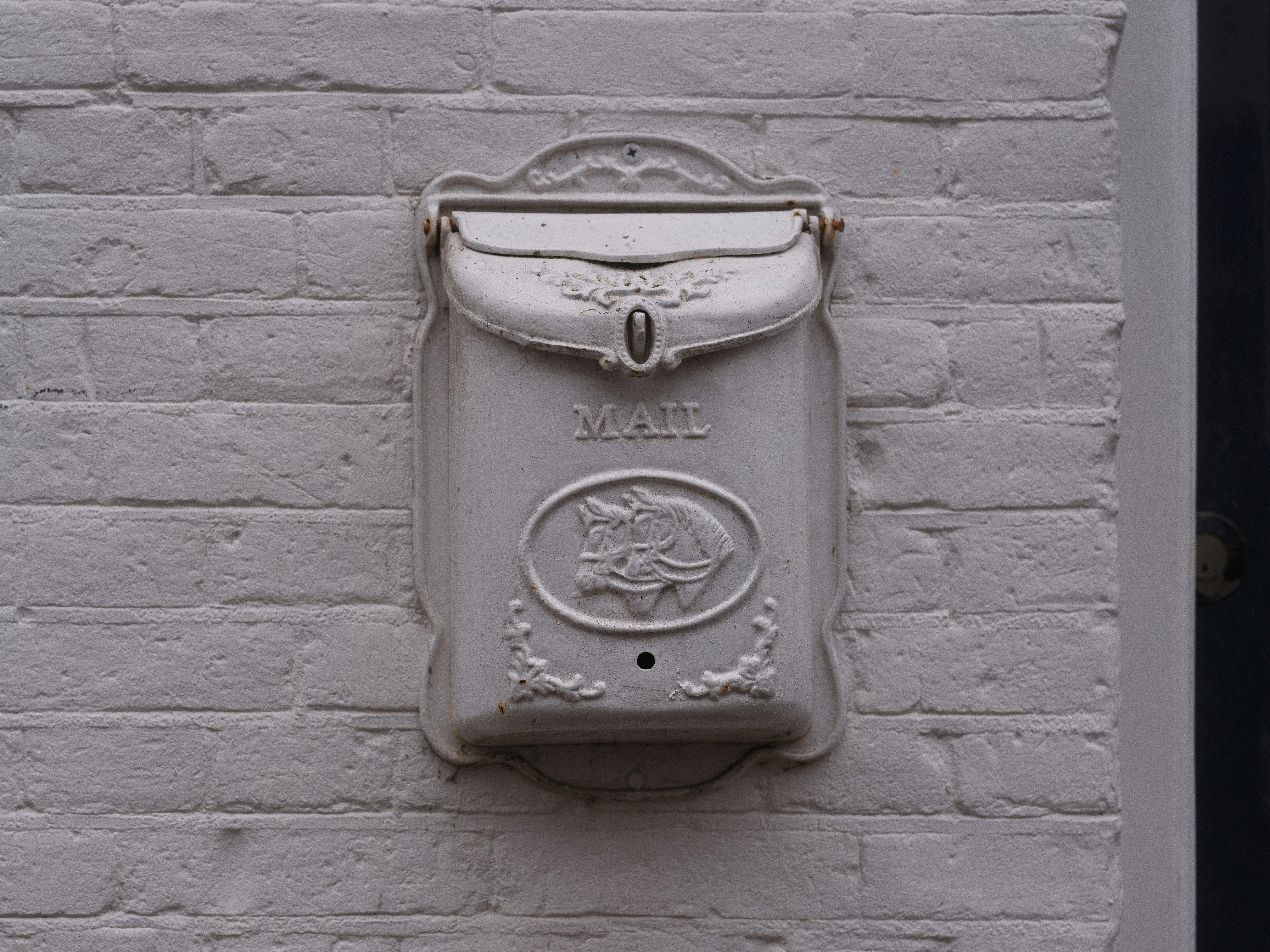 White ornate mailbox mounted on a brick wall
