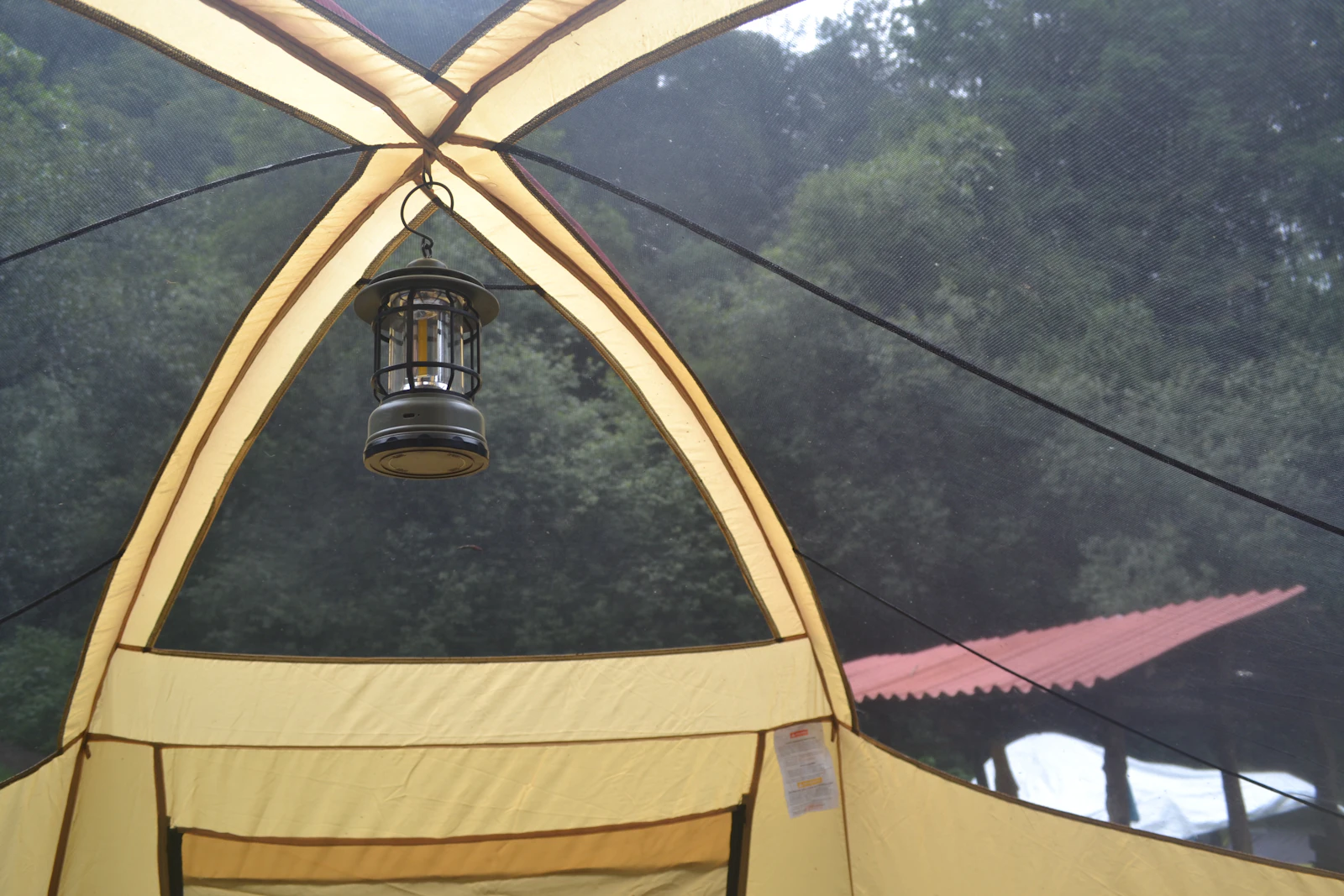Camping lantern hanging inside a tent with forest trees outside