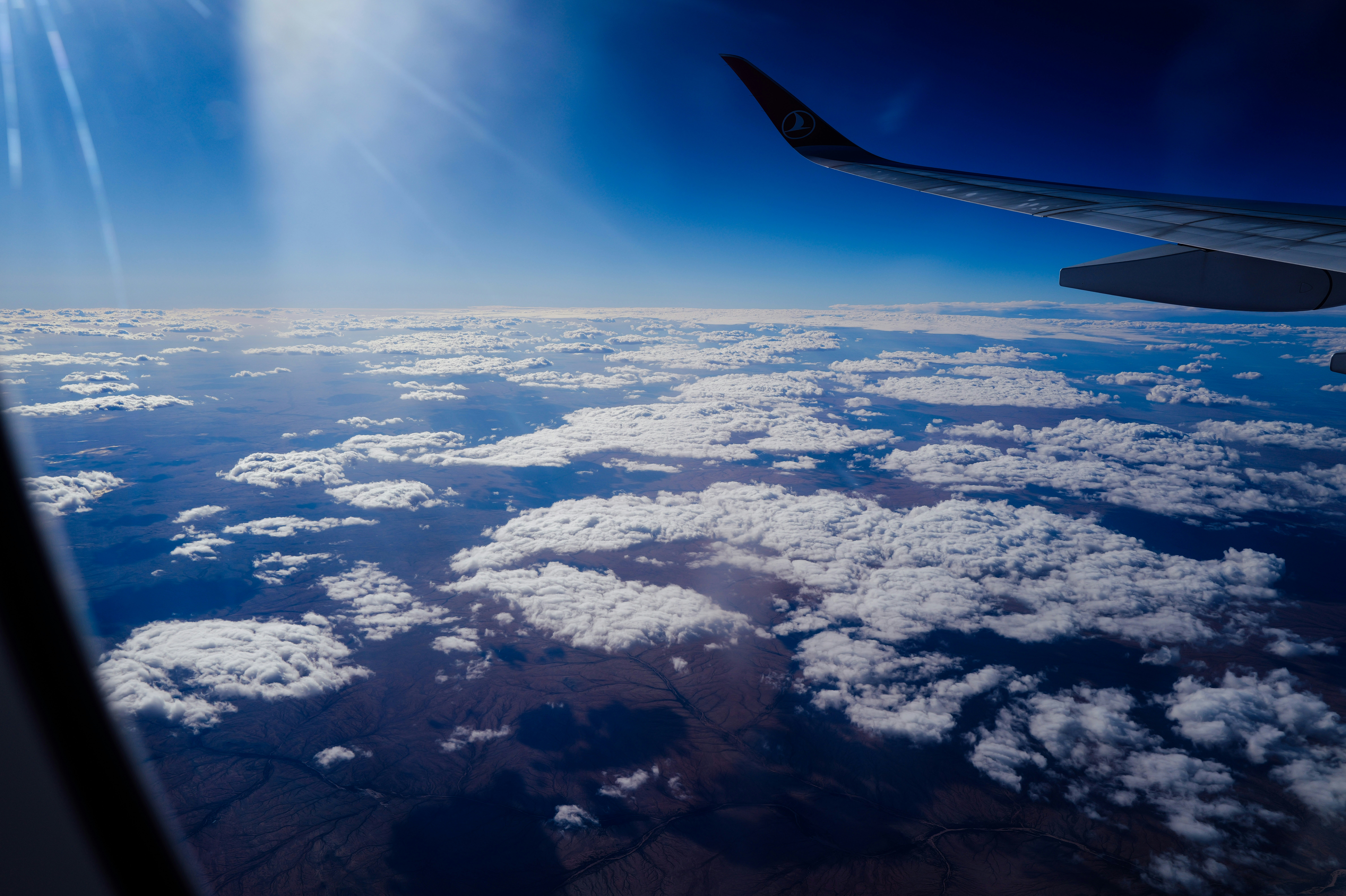View from airplane window of clouds and land below.