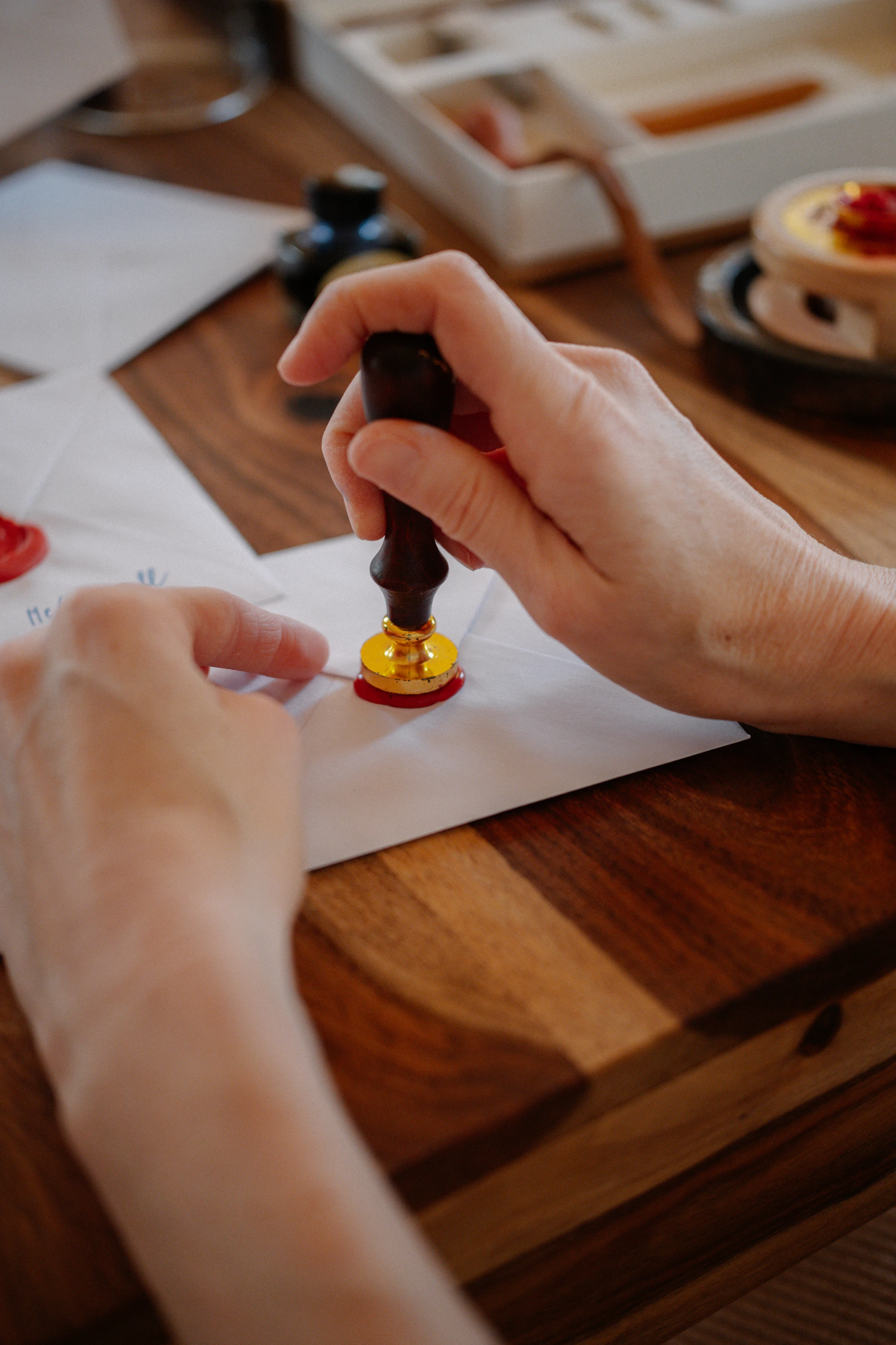Hands pressing a wooden-handled stamp into red wax on an envelope