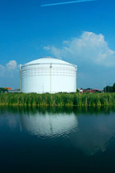 Large white storage tank by a calm body of water