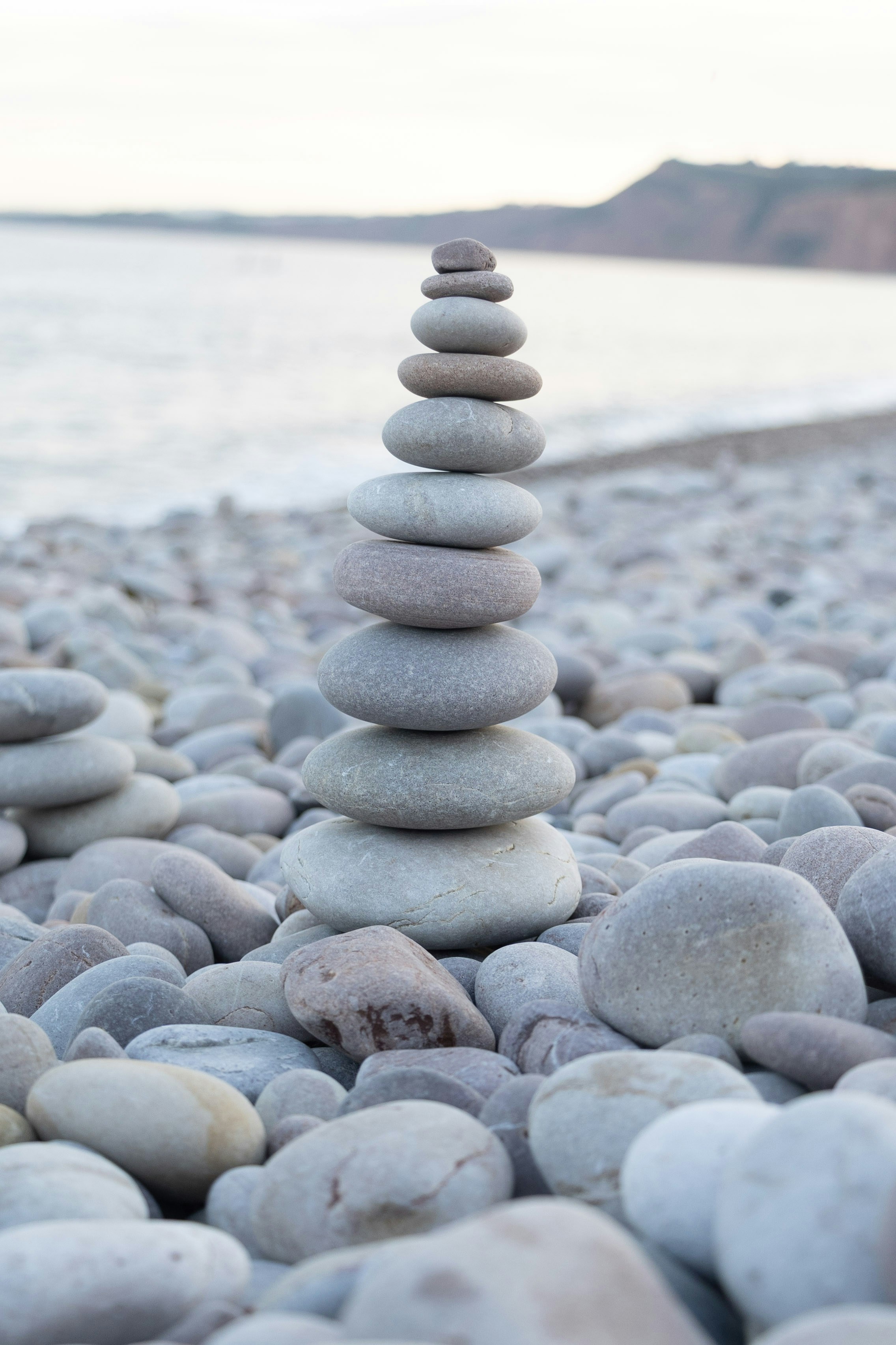 Gestapelte Steine auf einem Kiesstrand mit Meerhintergrund.