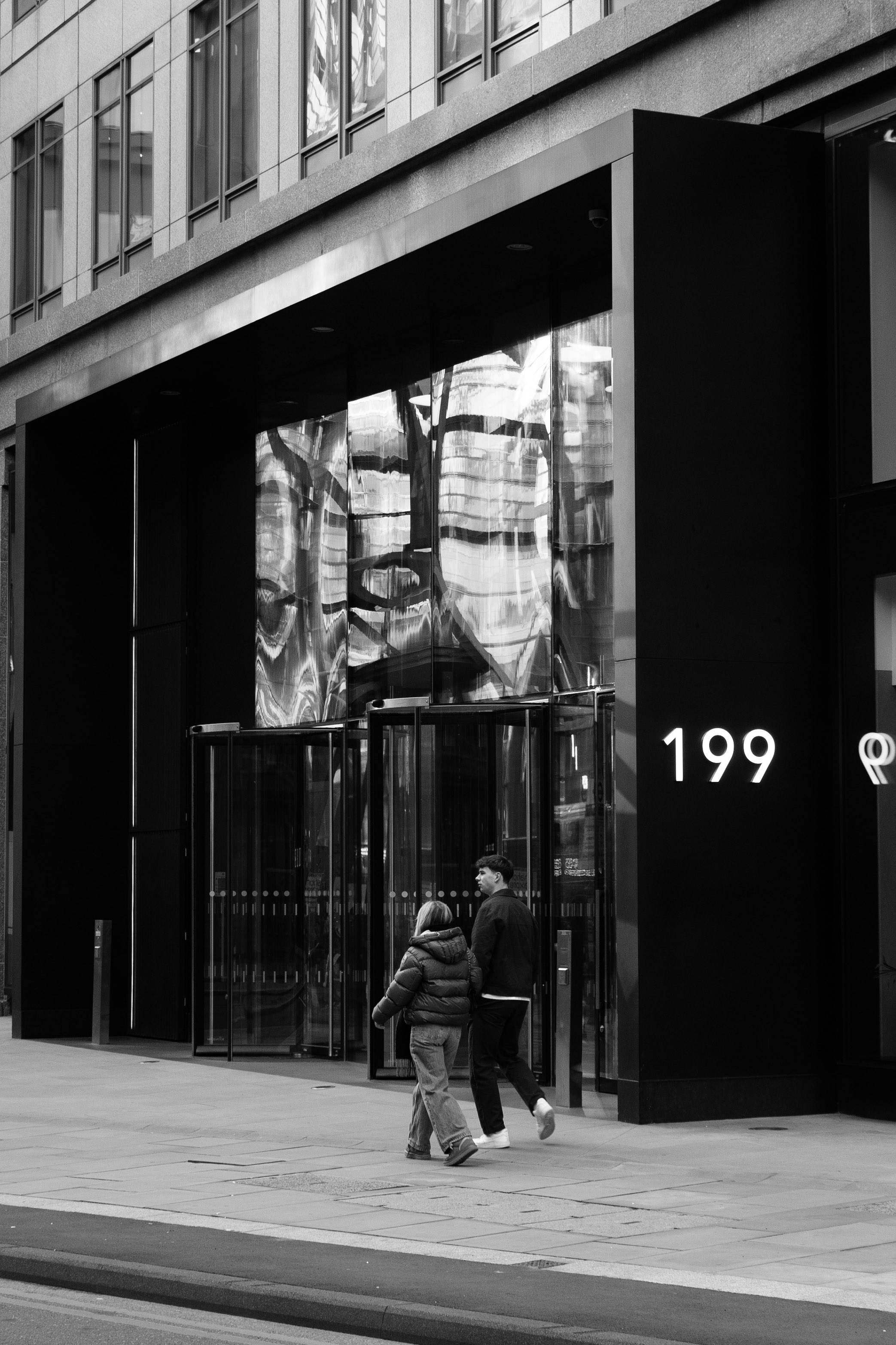 Zwei Personen gehen auf einen modernen Gebäudeeingang zu.