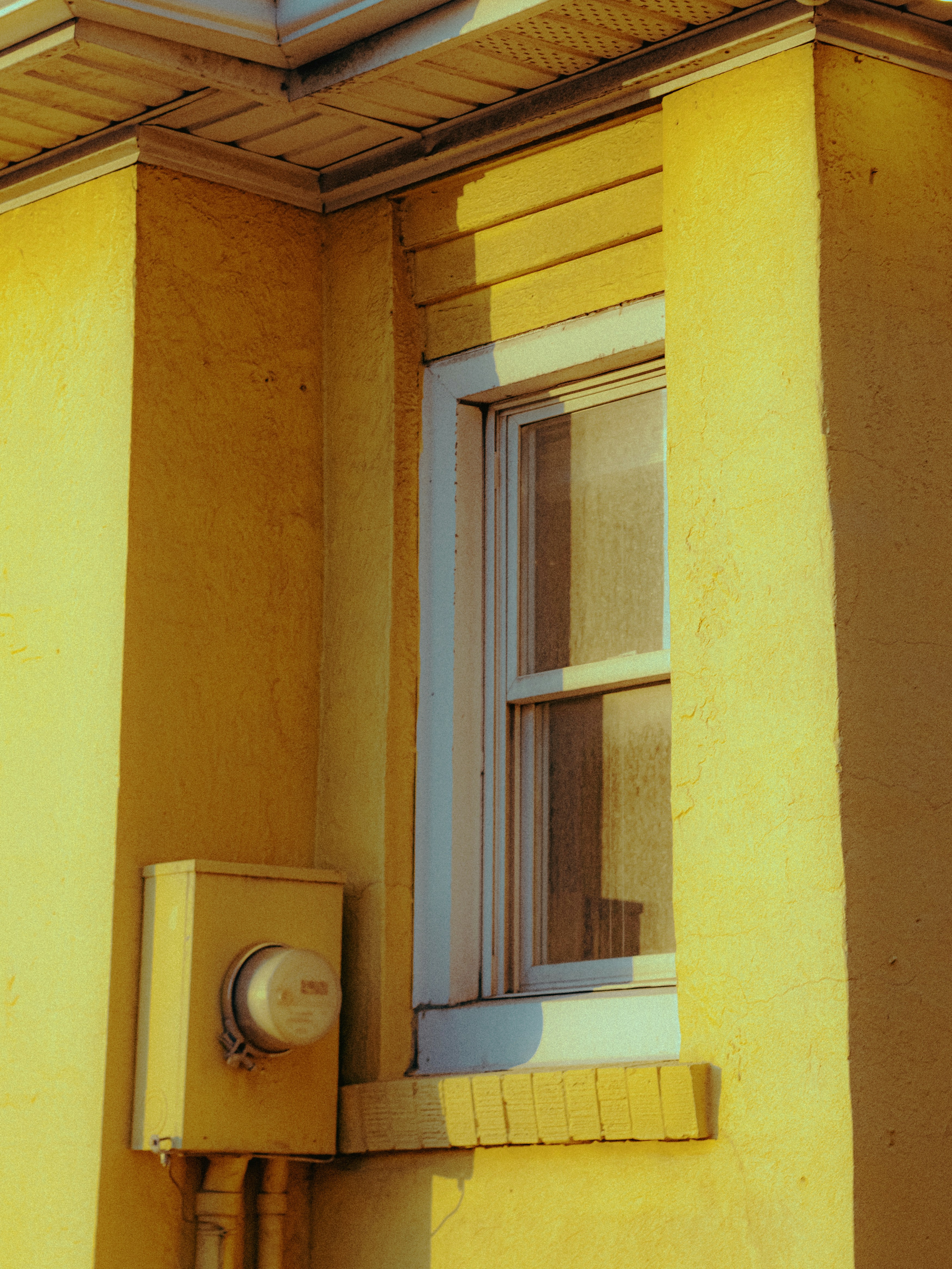 Yellow building exterior with a window and meter.