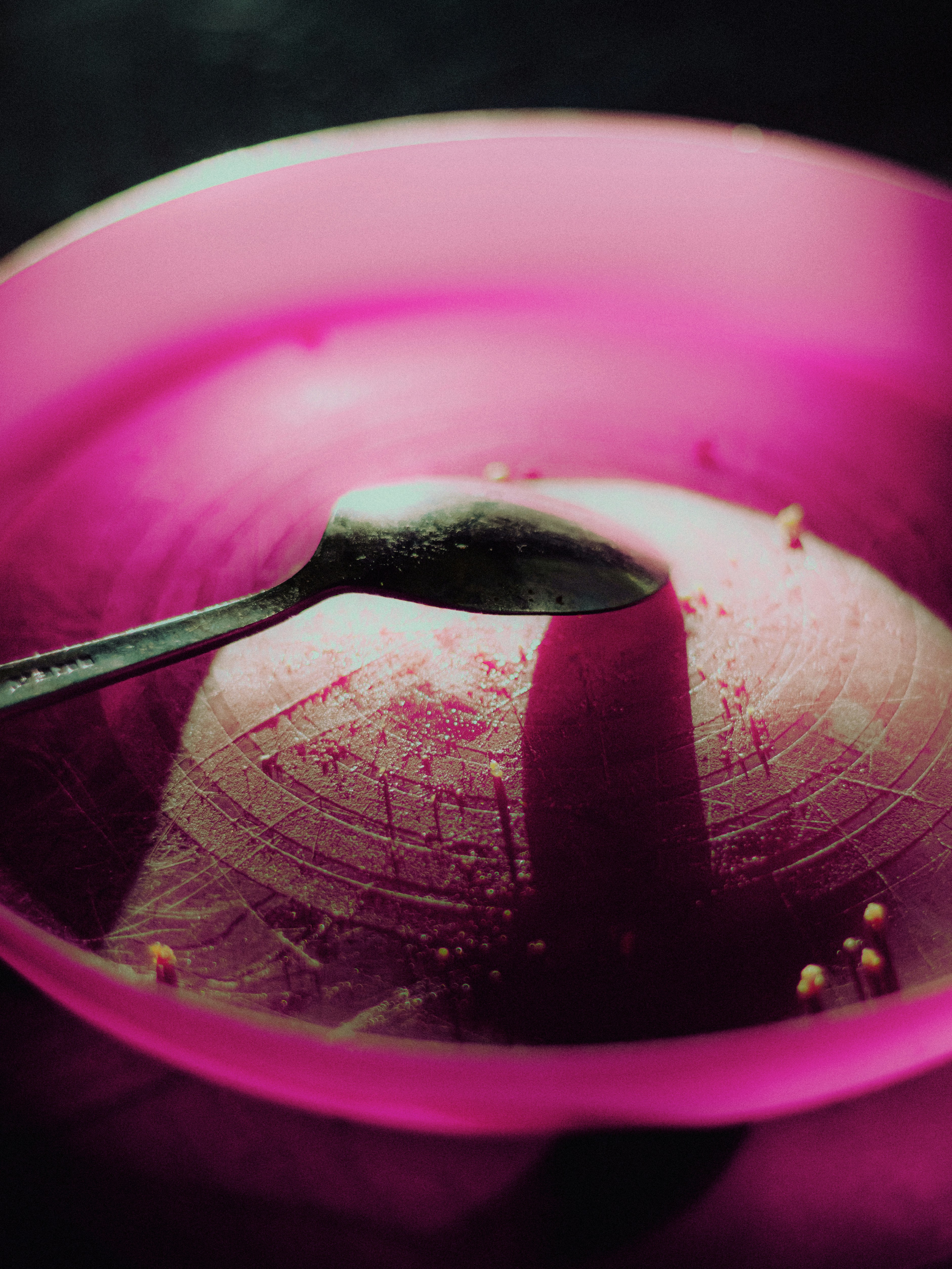A spoon rests in a pink bowl with scattered seeds.