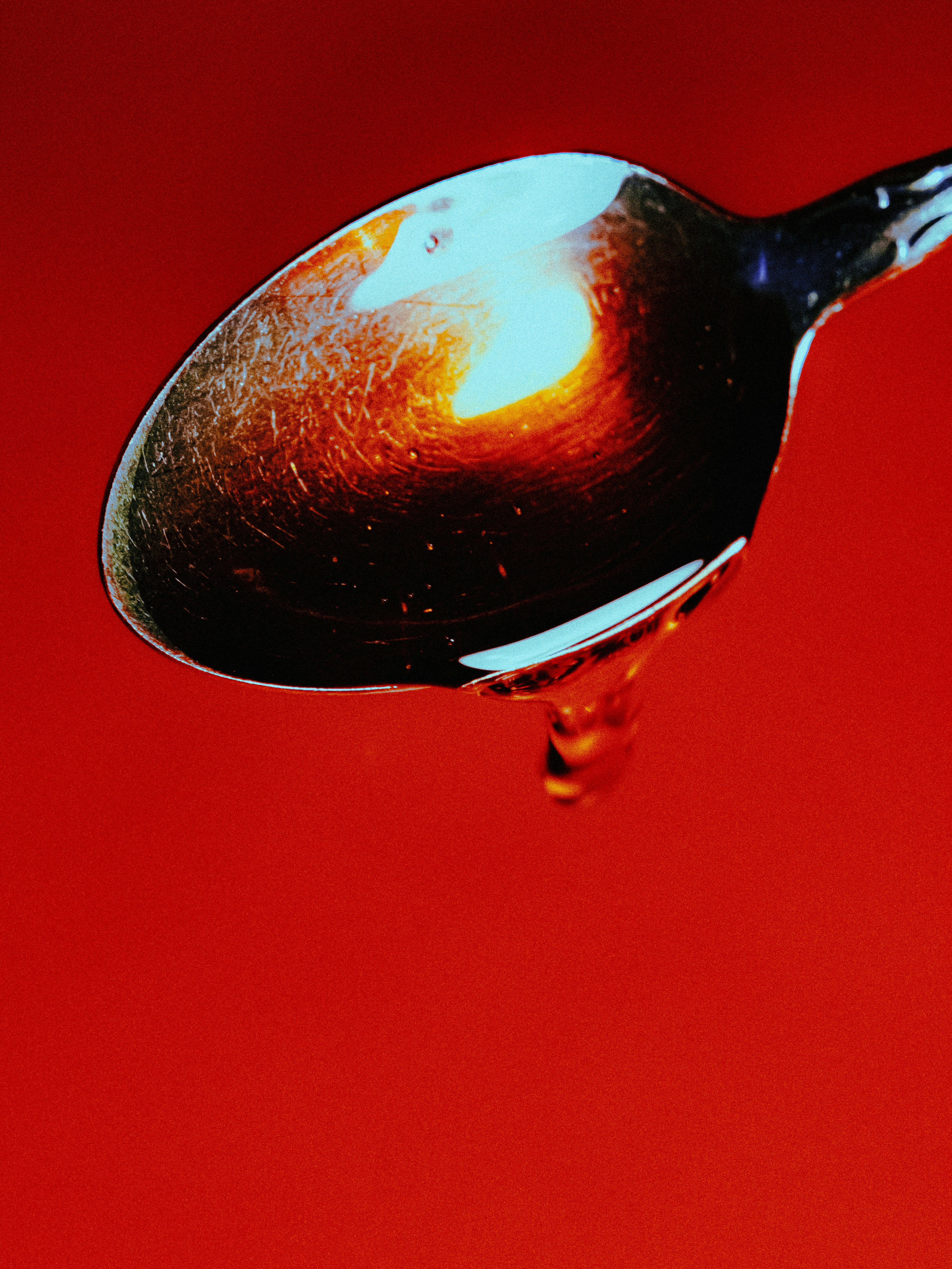 A spoon with honey dripping against a red background