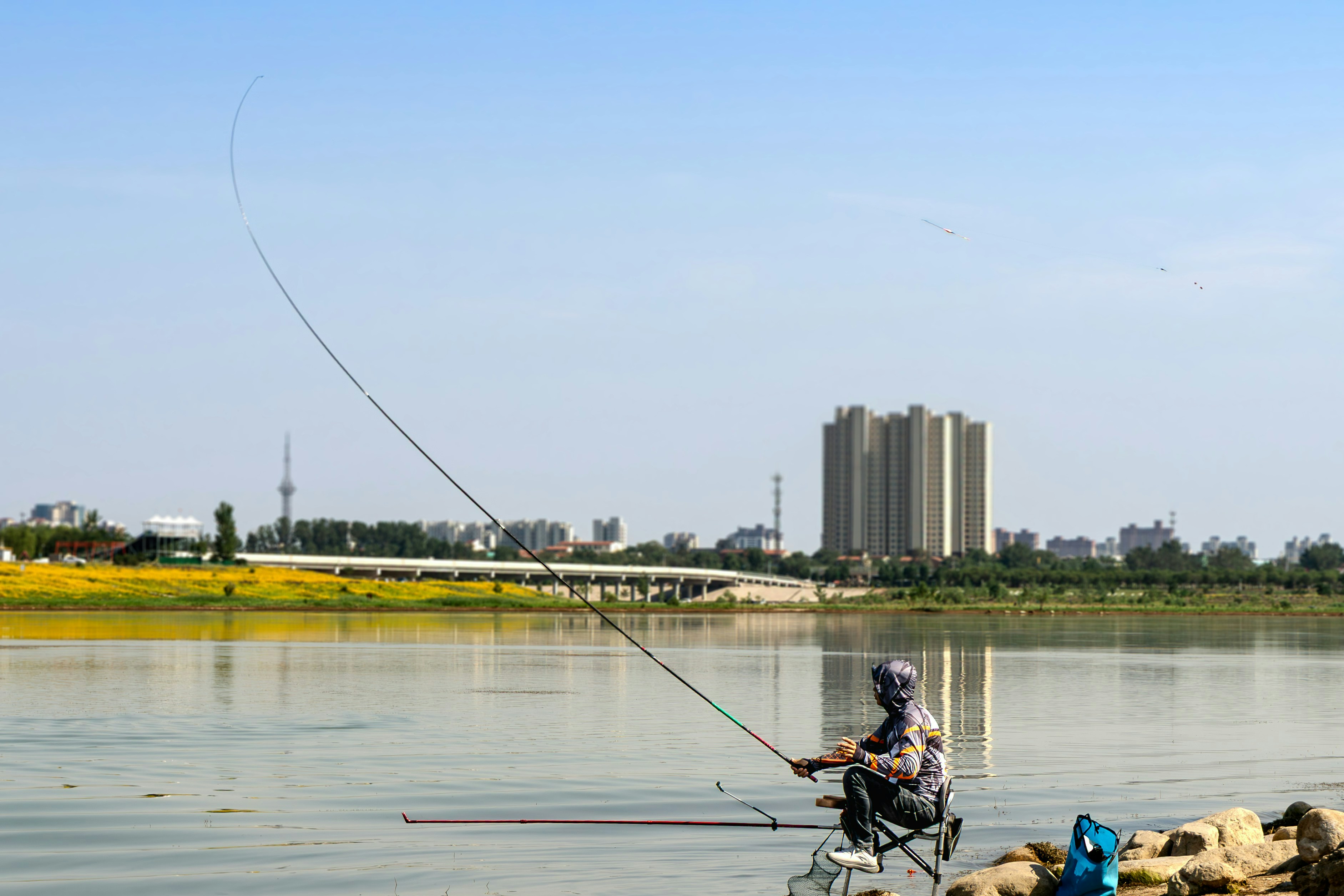 Pria memancing di tepi sungai yang tenang dengan bangunan kota
