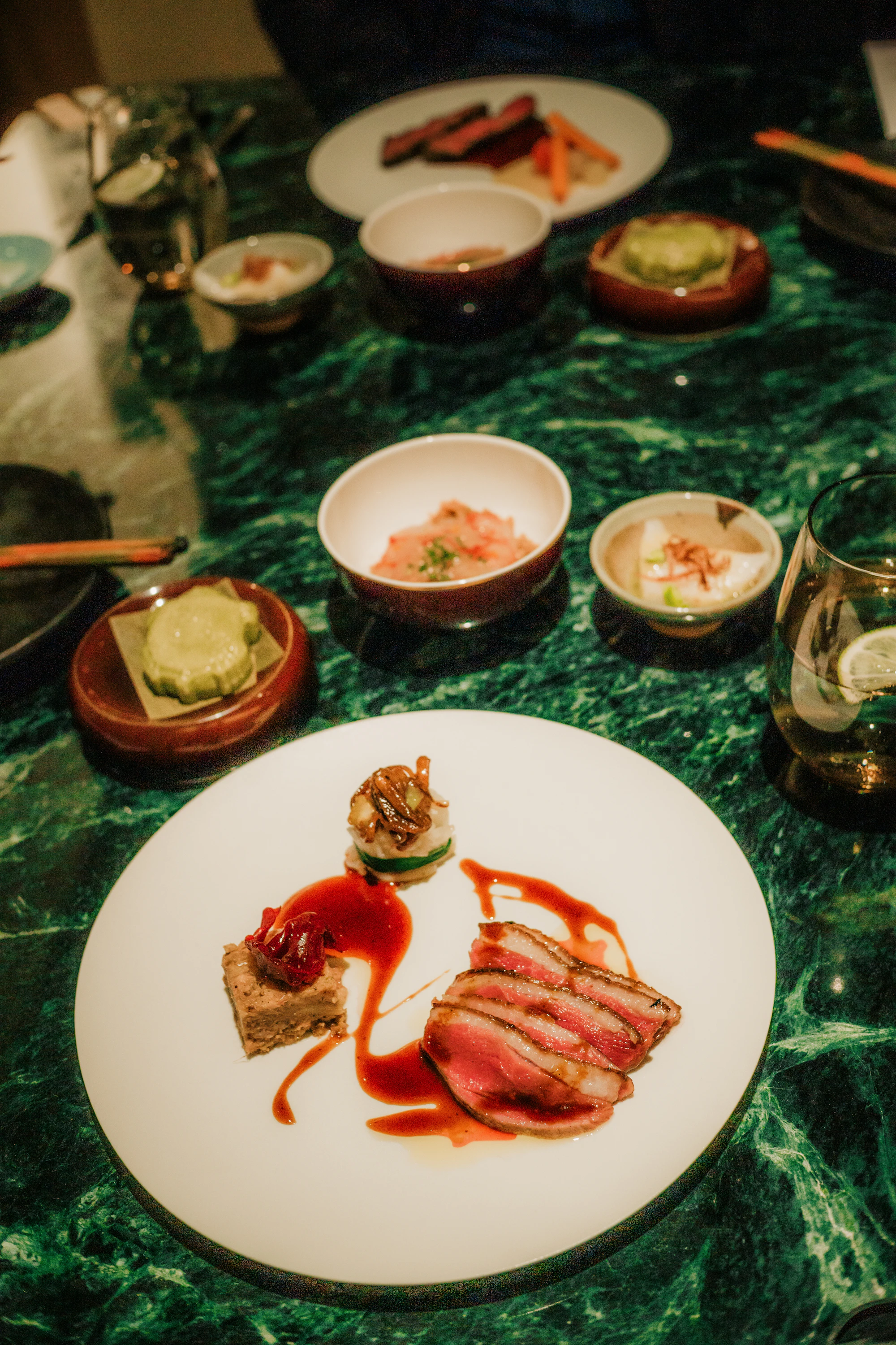 A candlelit fine-dining table set with precisely plated tasting courses in warm golden light.