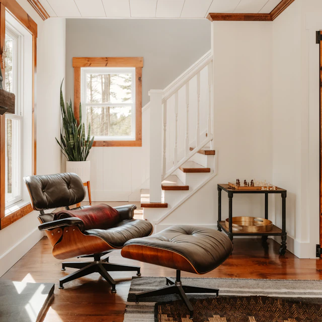 Cozy living room with an Eames lounge chair beside a fireplace, staircase and plants