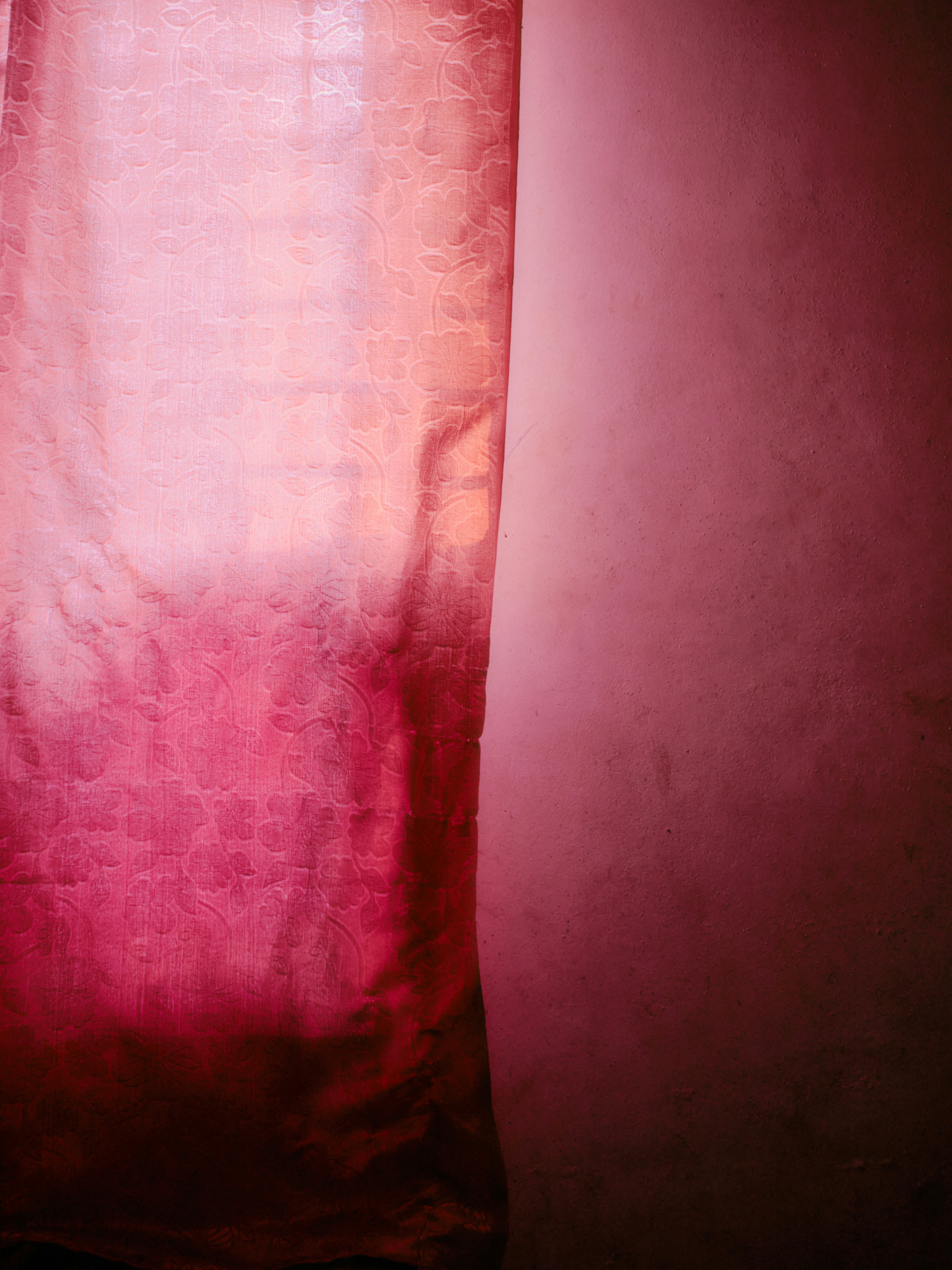Pink curtain with a textured pattern hangs by a wall.
