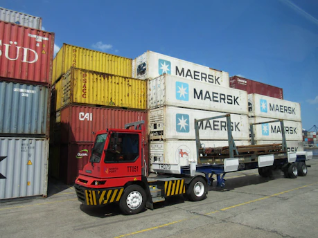 Red truck moving shipping containers at a port