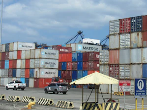 Stacked shipping containers at a busy port terminal.