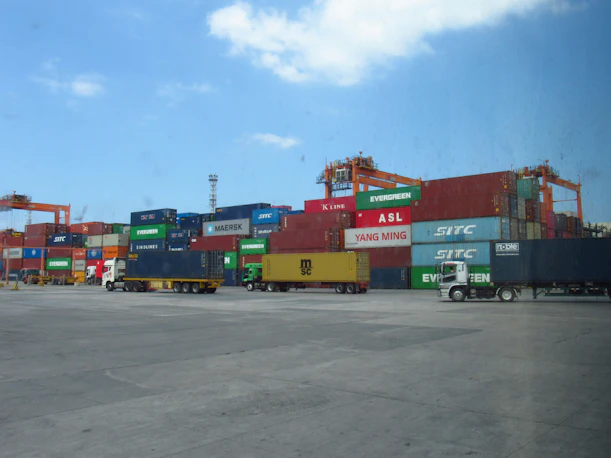 Shipping containers stacked at a busy port with trucks