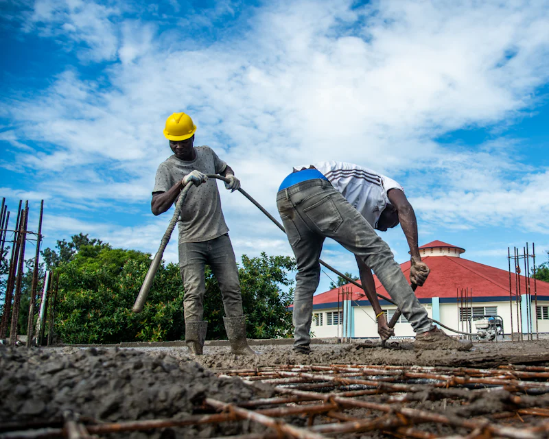 Two workers smoothing fresh concrete over rebar in bright sunlight