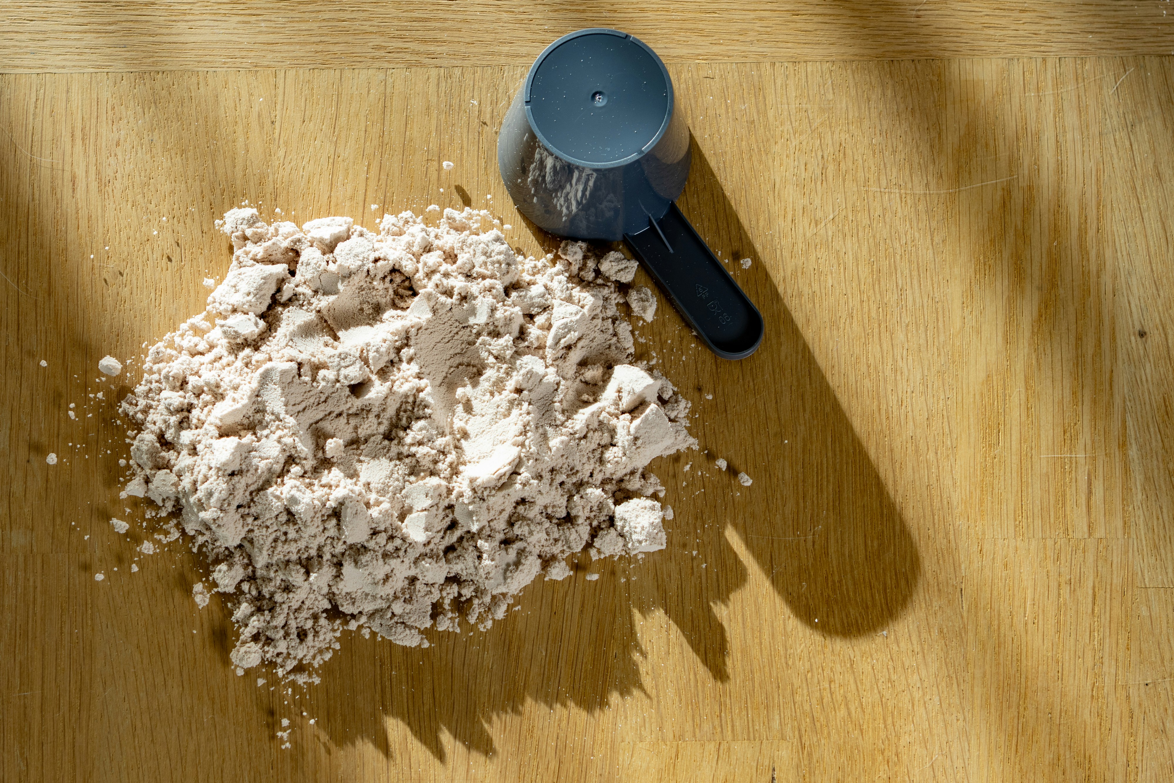 Scoop of protein powder on a wooden surface