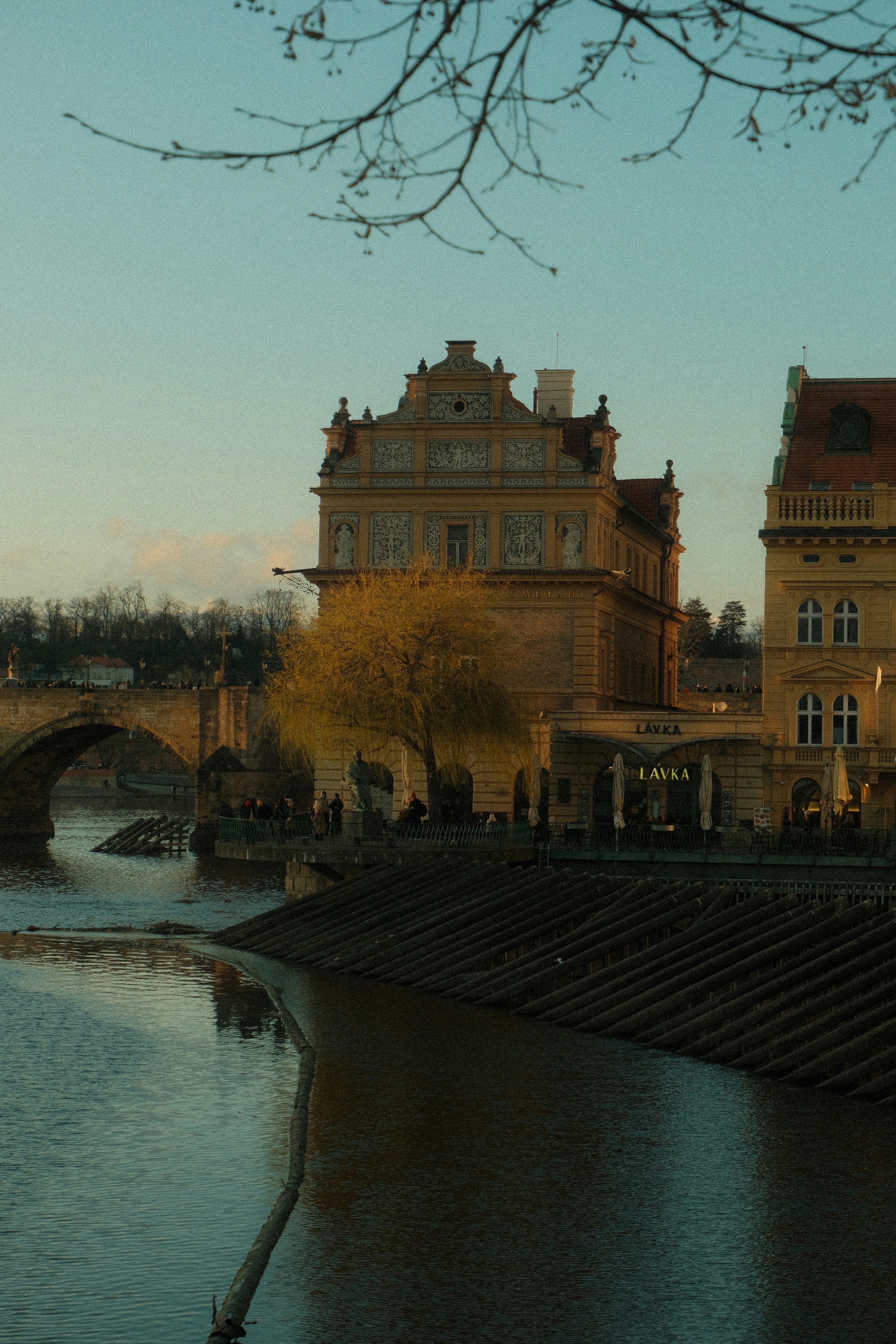 Historic buildings line a river with a bridge.