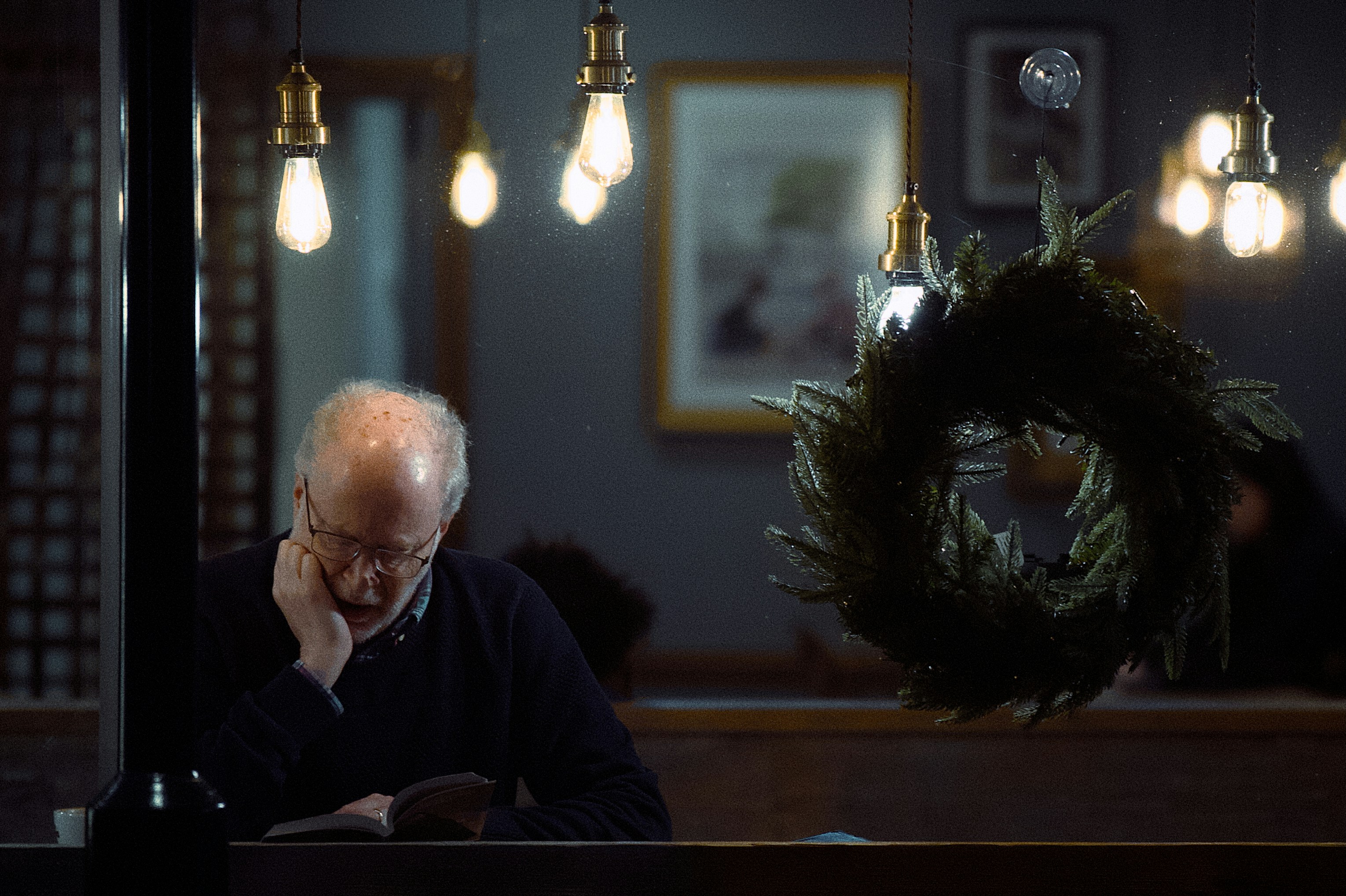 Elderly man reading a book in a dimly lit room.