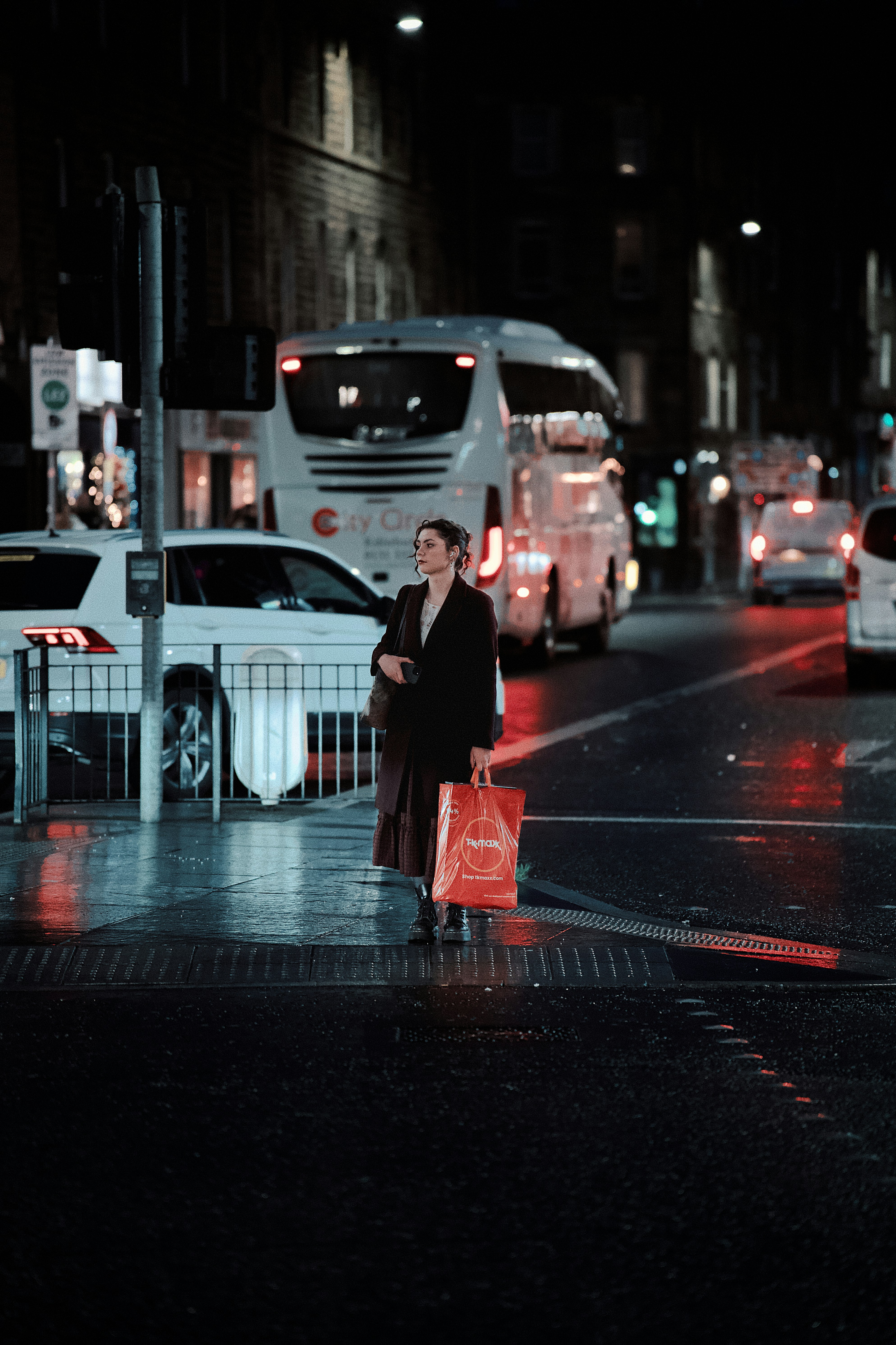 Woman waiting at a wet city street crossing at night