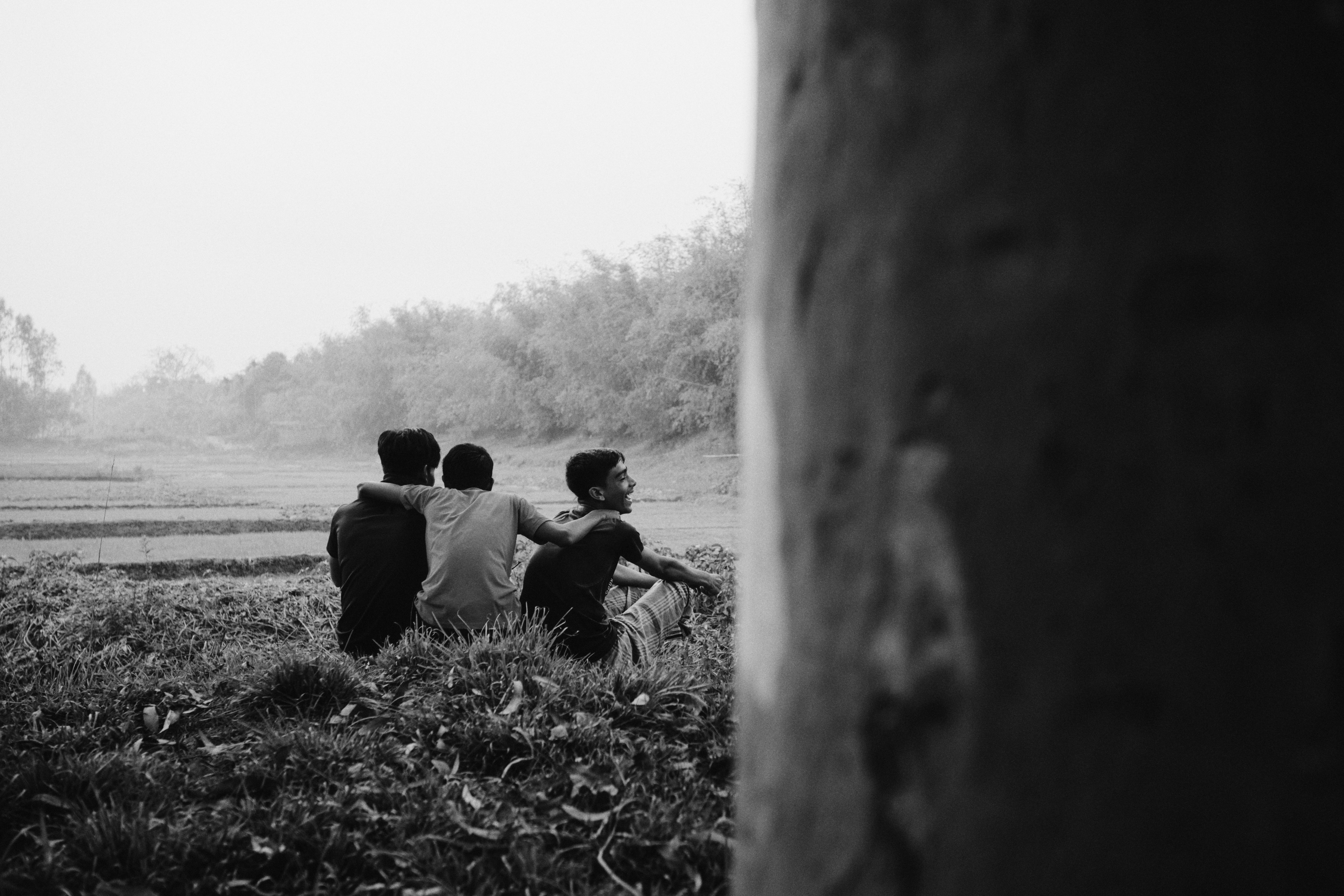 Three boys sitting in a field looking away.
