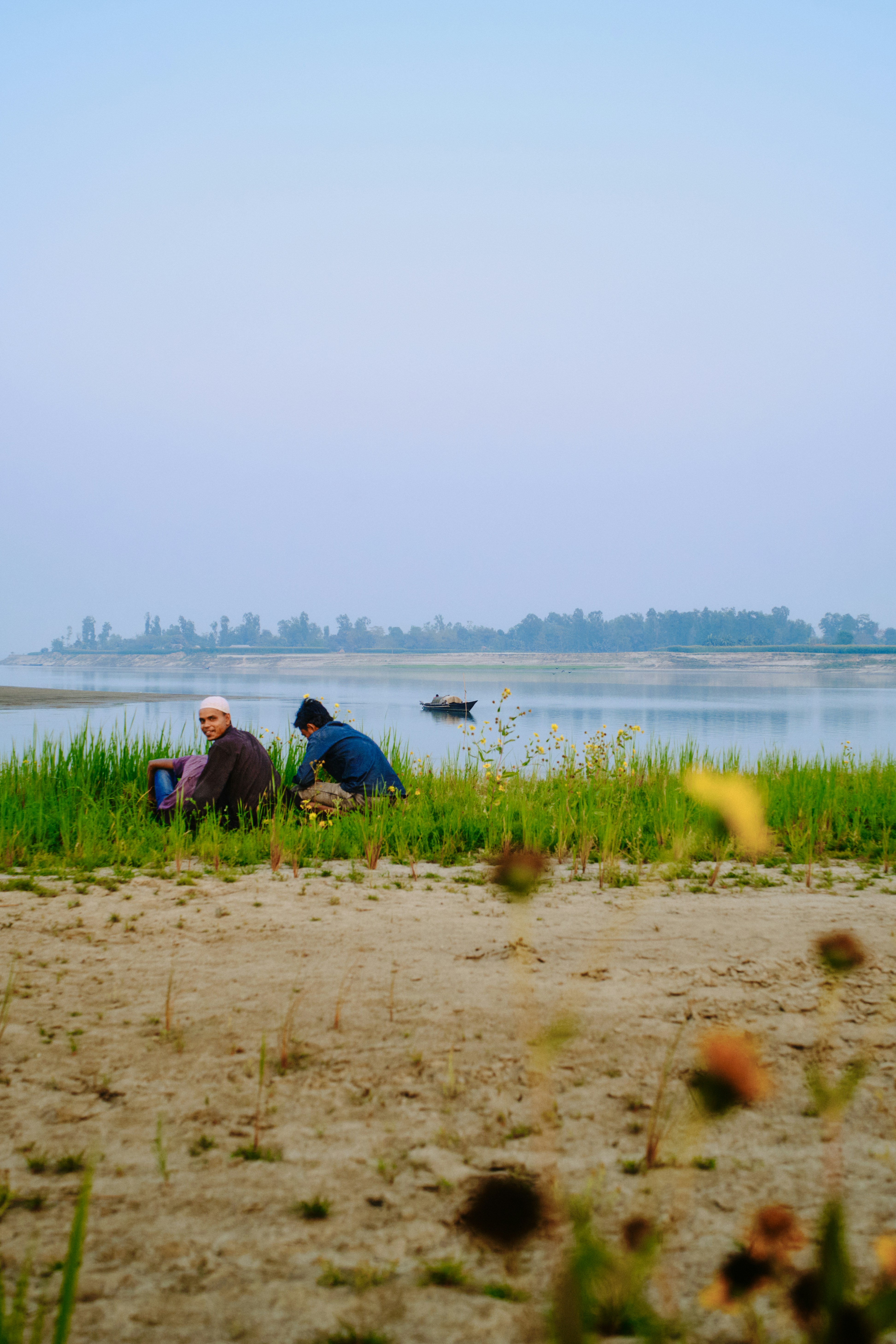 Two men sitting by a calm riverbank at dawn.