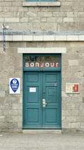 Teal double doors with "bonjour" sign above