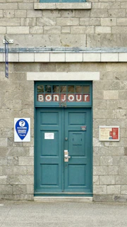 Teal double doors with "bonjour" sign above
