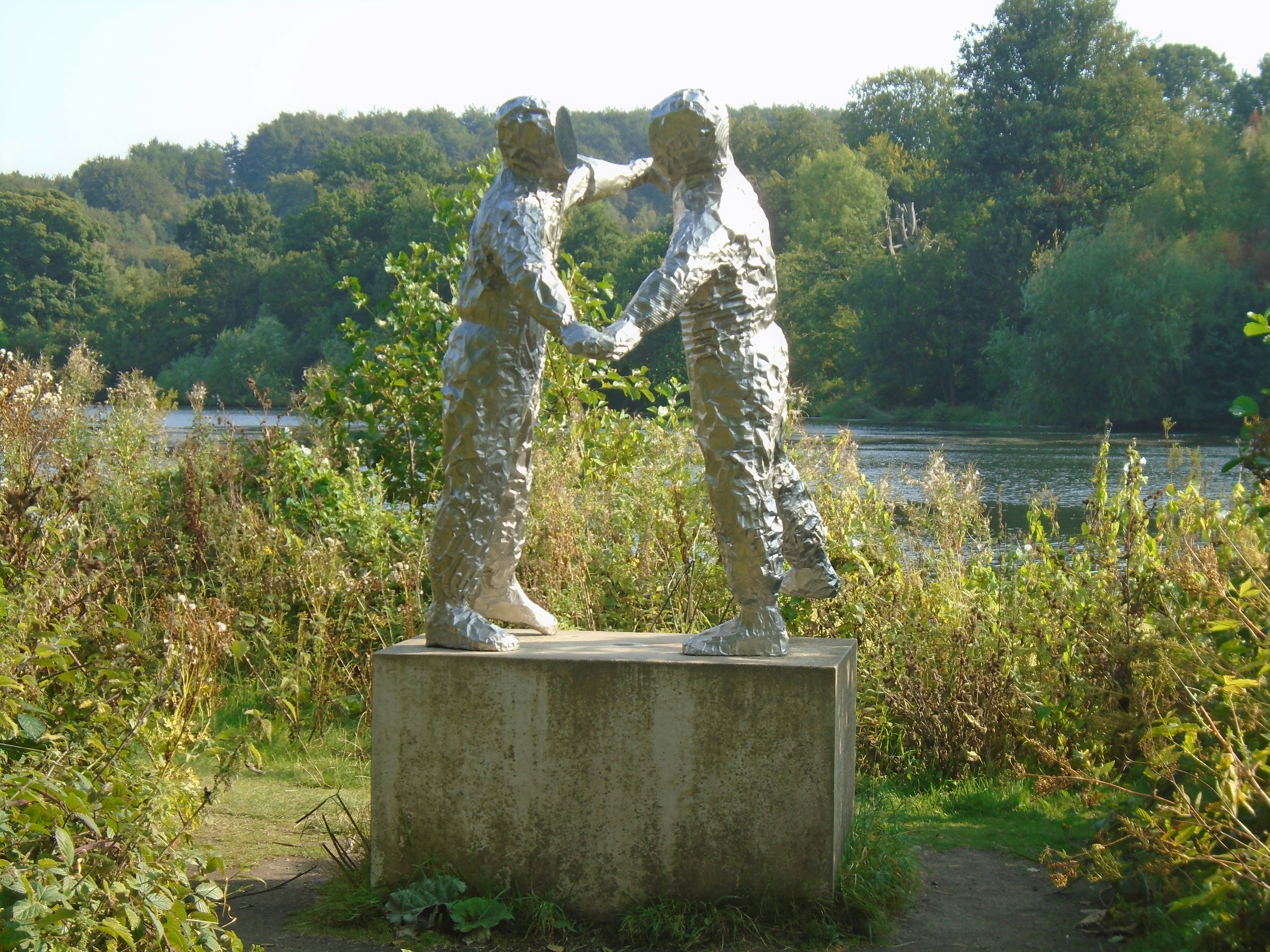 Due figure in una scultura metallica accanto a un lago.