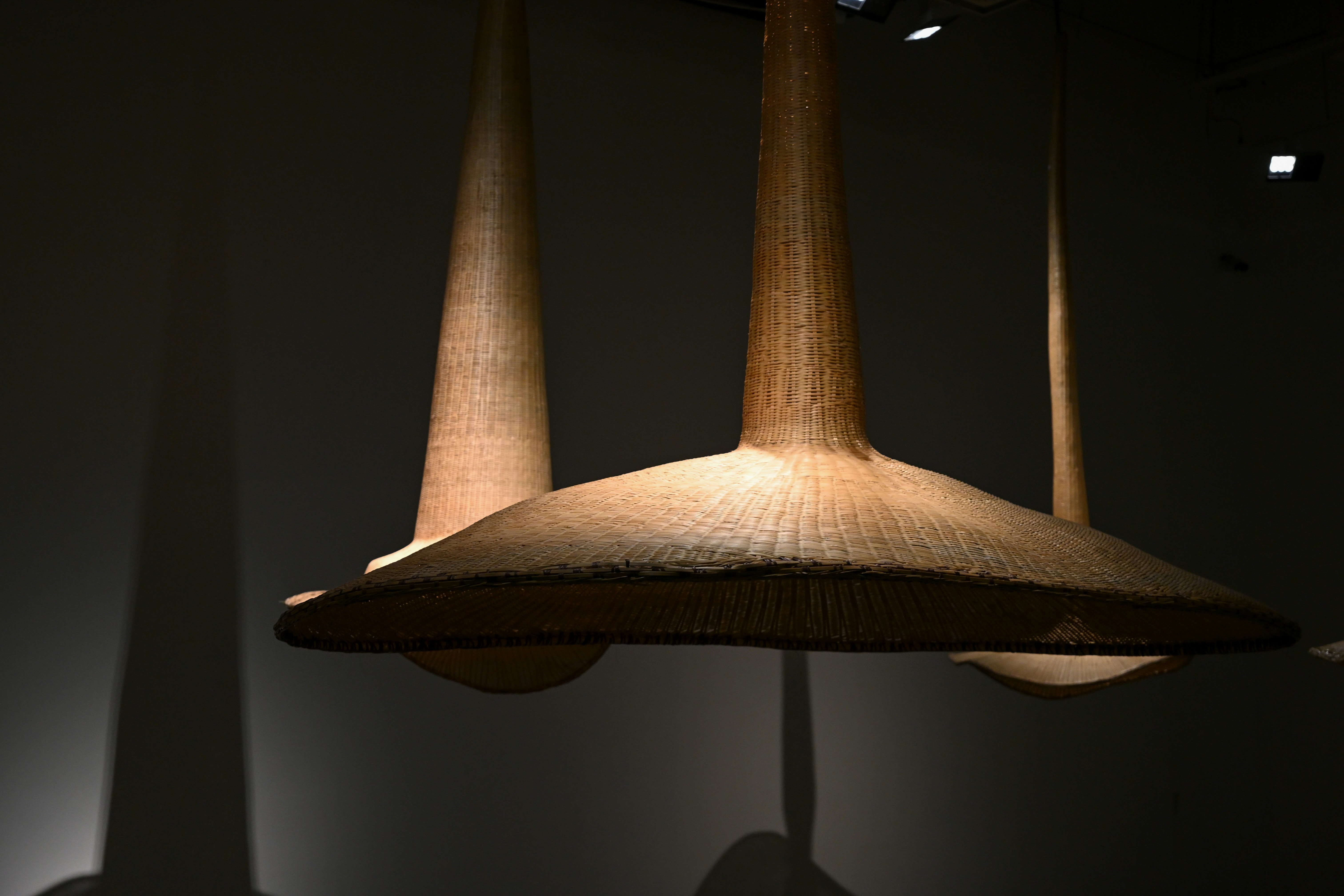 Trois lampes coniques tissées pendent dans l’obscurité.