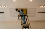 Man on ladder working on ceiling access panel.
