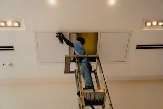 Man on ladder working on ceiling access panel.