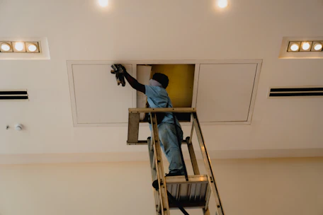 Man on ladder working on ceiling access panel.