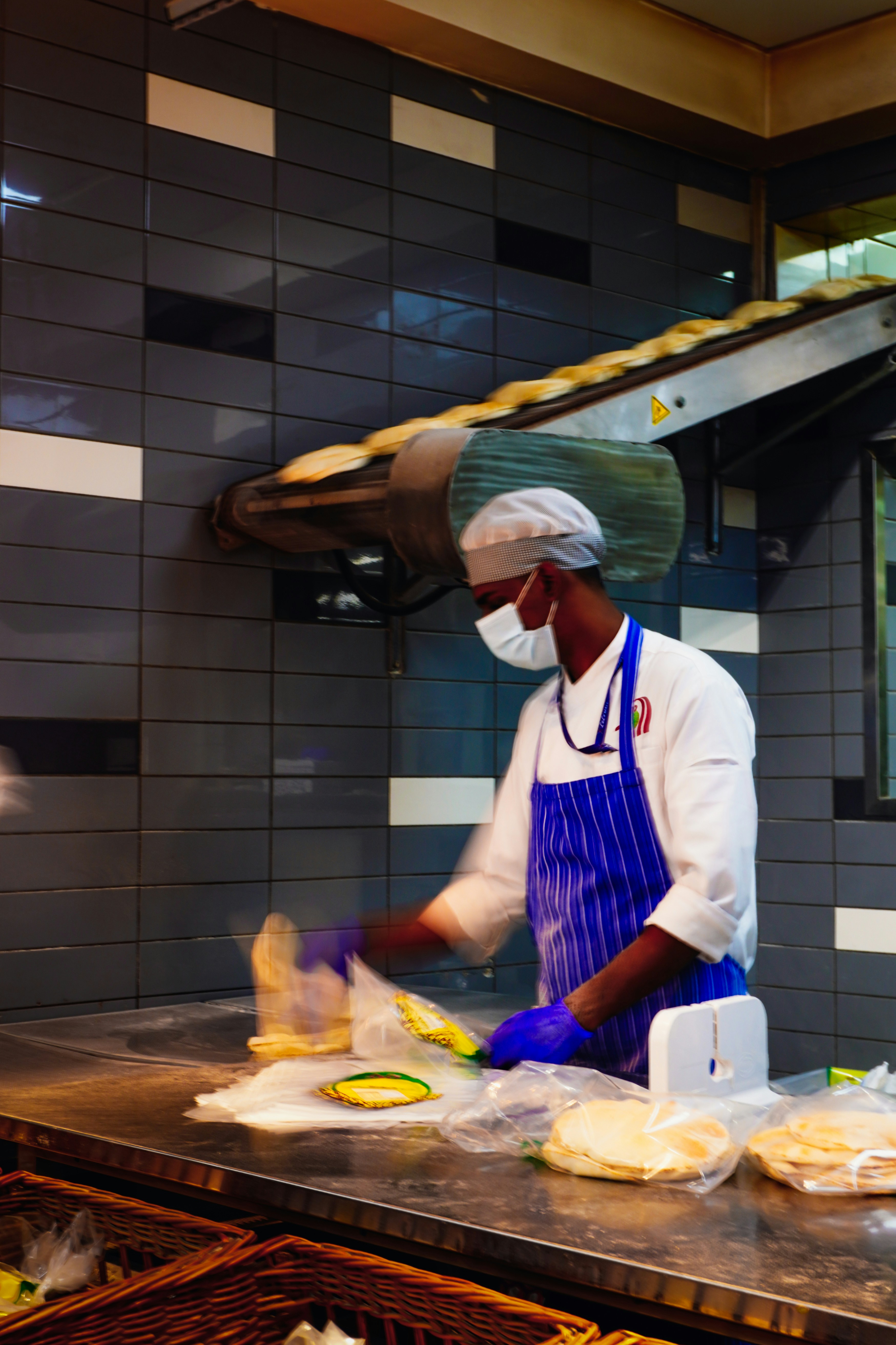 Panadero con máscara prepara la masa en una cocina.