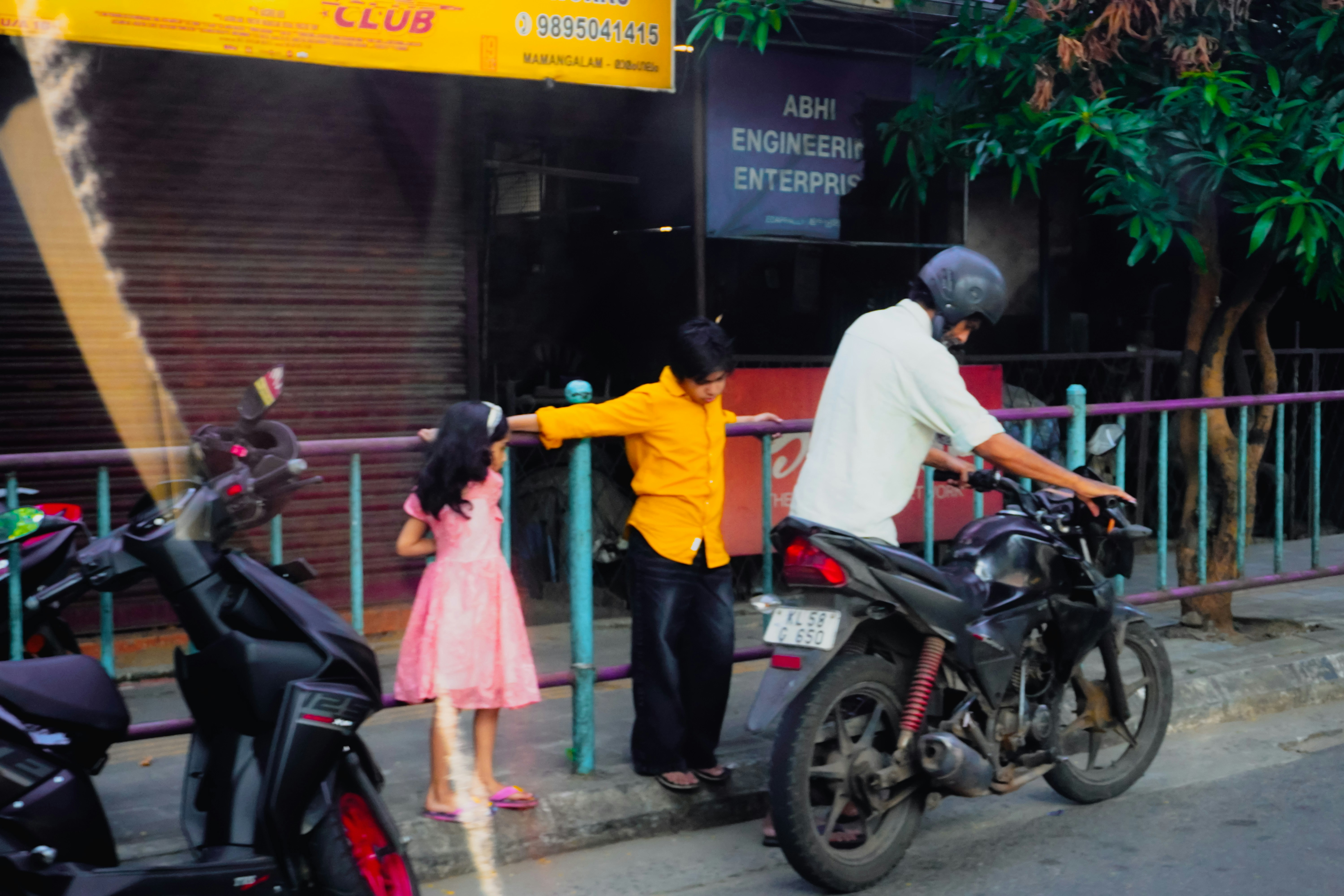 Pria di atas sepeda motor mengawasi anak-anak dengan pagar.