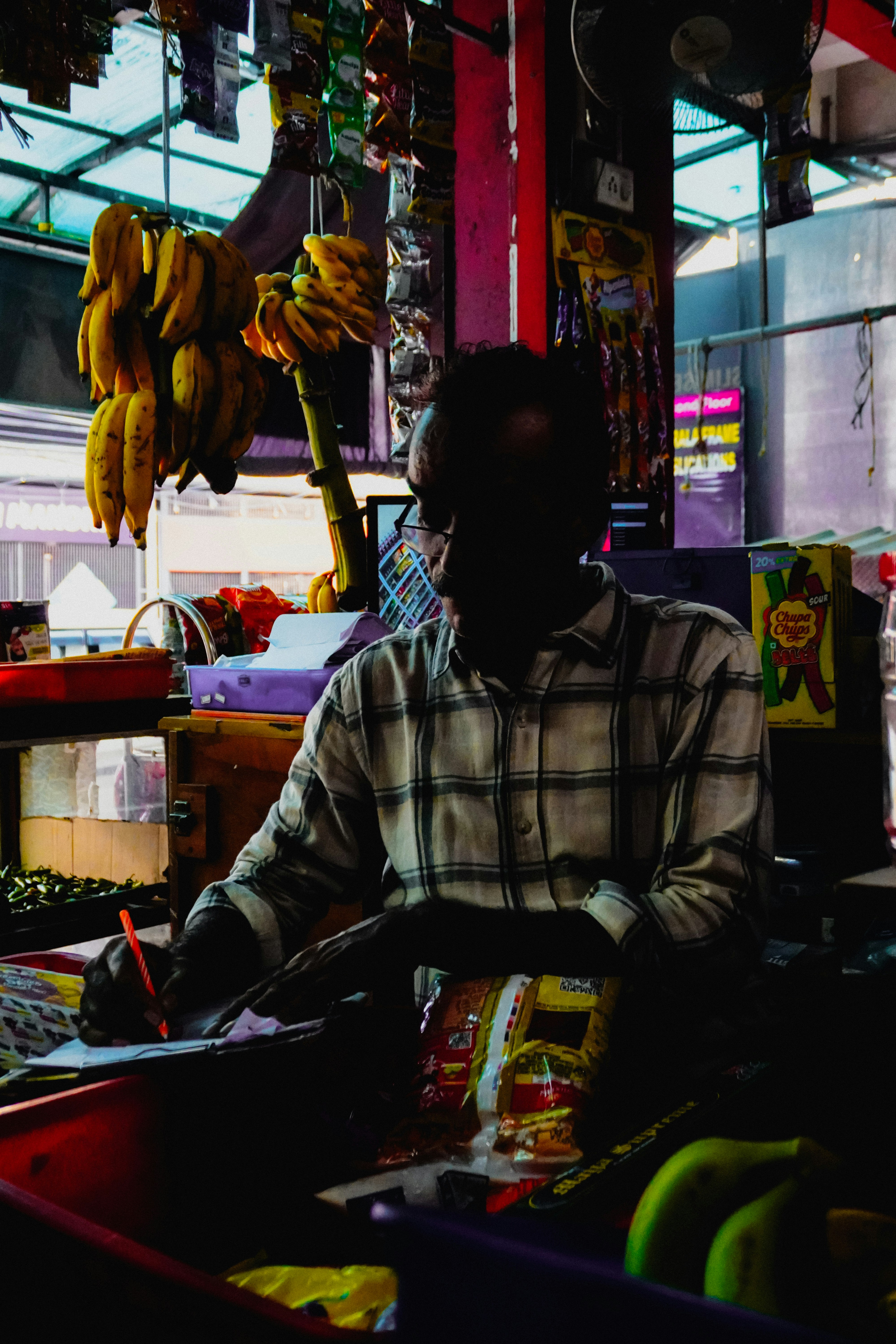 Man in plaid shirt writing at a market stall.