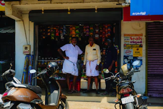 Two men stand outside a small shop with motorcycles.